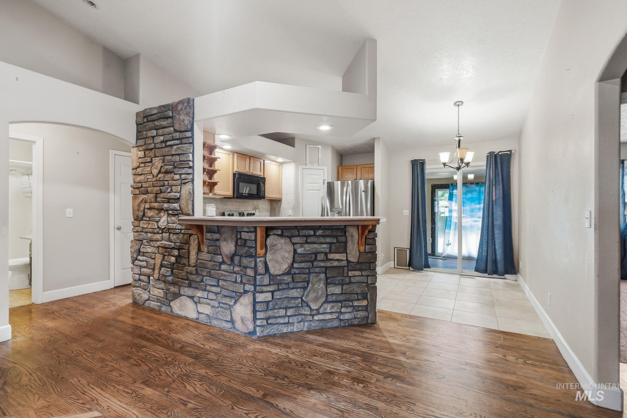 Stone-faced kitchen island with a breakfast bar, featuring wood-finish flooring, recessed lighting, and a kitchen with wood cabinetry