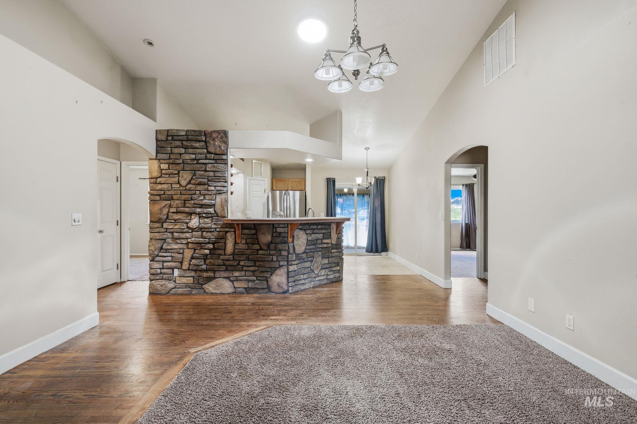 Spacious interior featuring vaulted ceilings, a stone-clad breakfast bar, wood-finish flooring, and arched doorways