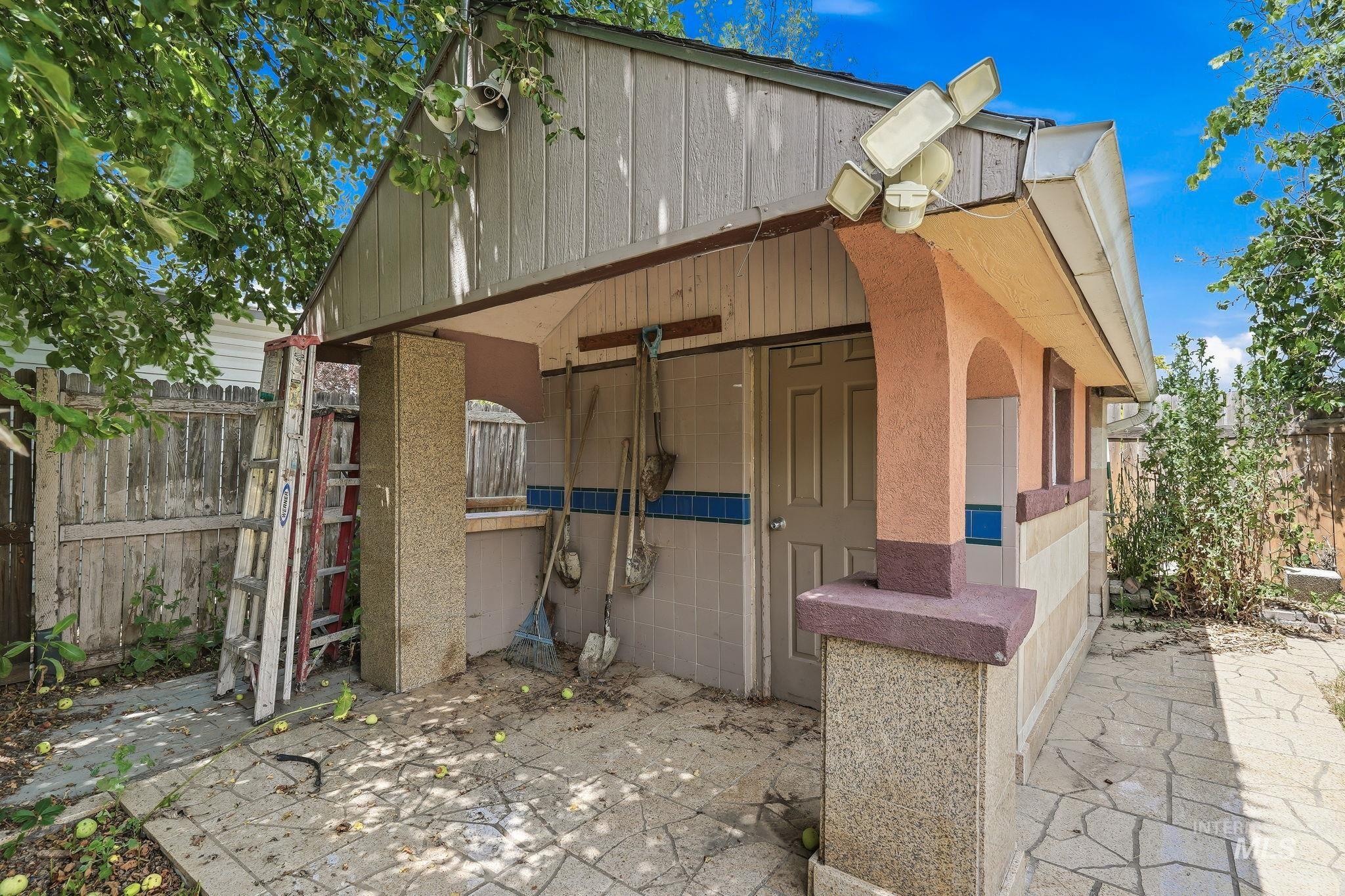 Outdoor storage structure featuring a covered patio, tiled flooring, stucco archways, and exterior lighting fixtures