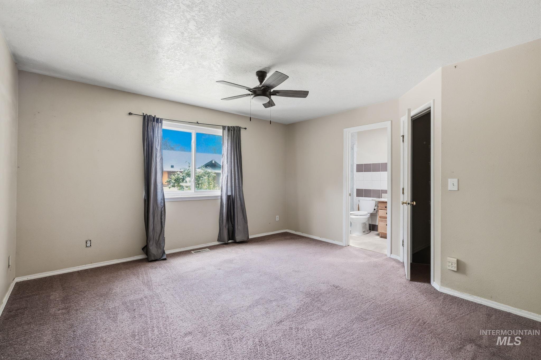 Spacious room with plush carpeting, a ceiling fan with light fixture, and a window with curtains