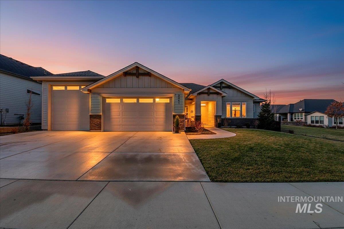 Craftsman-style house with board and batten siding, driveway, a front yard, an attached garage, and stone siding