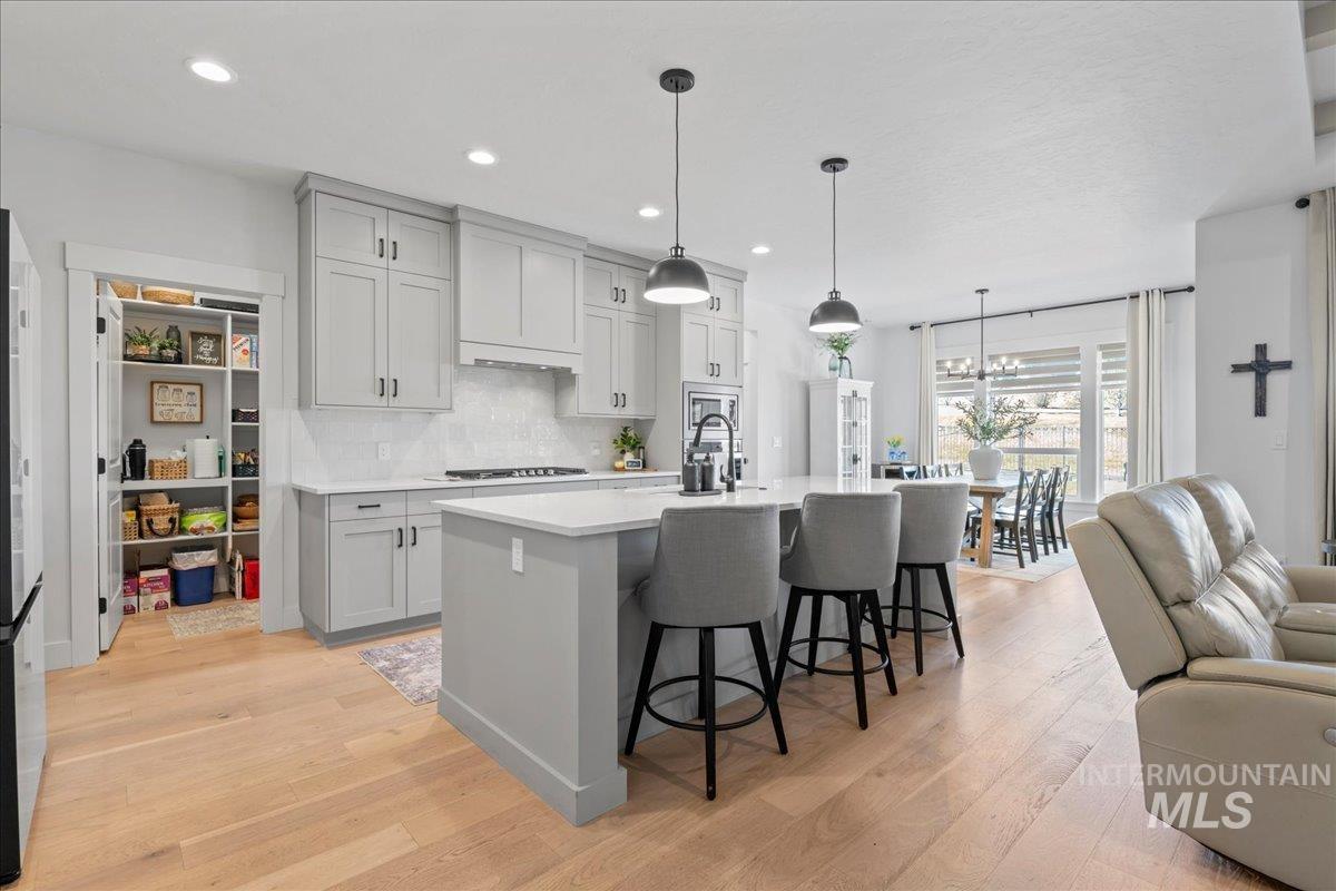 Kitchen with open floor plan, a kitchen breakfast bar, light wood-type flooring, a center island with sink, and tasteful backsplash