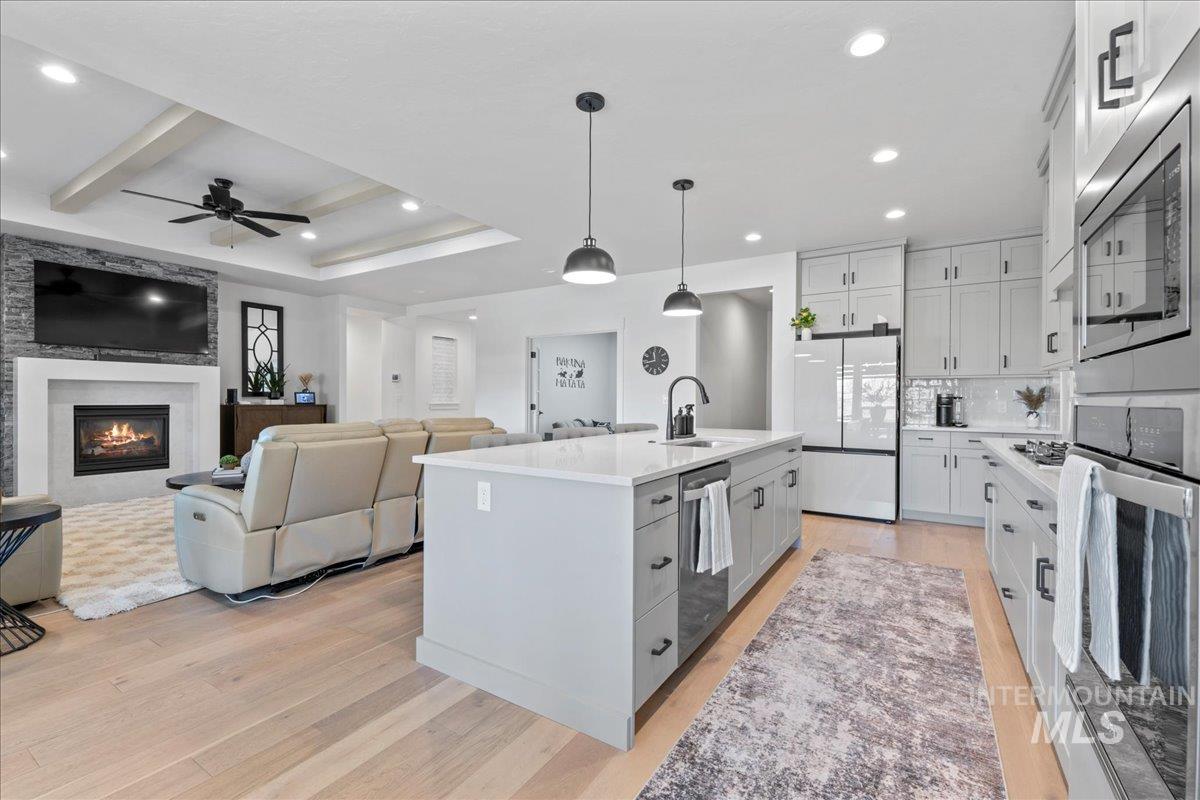 Kitchen with stainless steel appliances, pendant lighting, a center island with sink, light wood-style floors, and beam ceiling