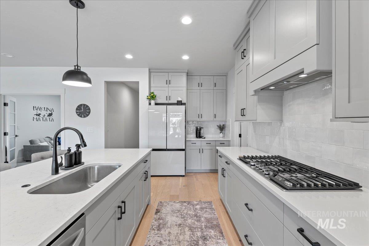 Kitchen featuring pendant lighting, light wood-style flooring, freestanding refrigerator, stainless steel gas cooktop, and light stone countertops