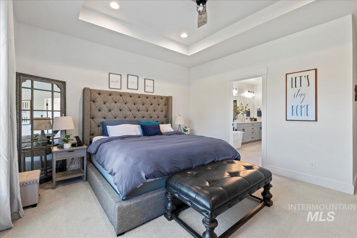 Bedroom featuring light colored carpet, recessed lighting, a tray ceiling, and ensuite bath