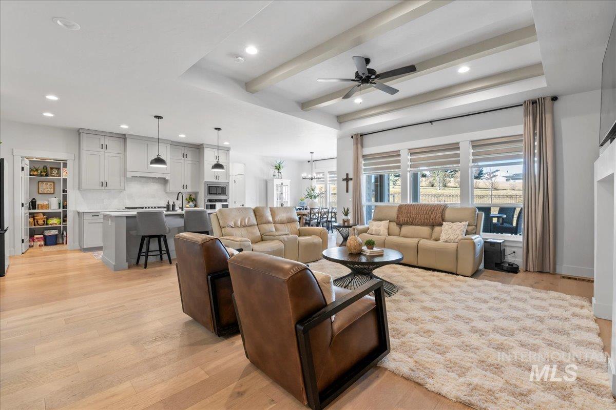 Living area with a ceiling fan, light wood-style flooring, recessed lighting, a tray ceiling, and beamed ceiling