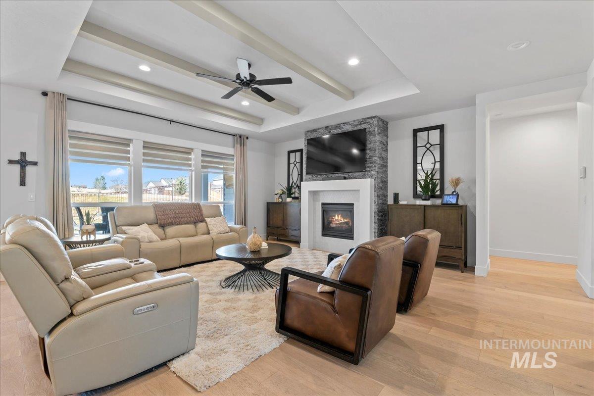 Living area featuring ceiling fan, light wood-style flooring, recessed lighting, a large fireplace, and a raised ceiling