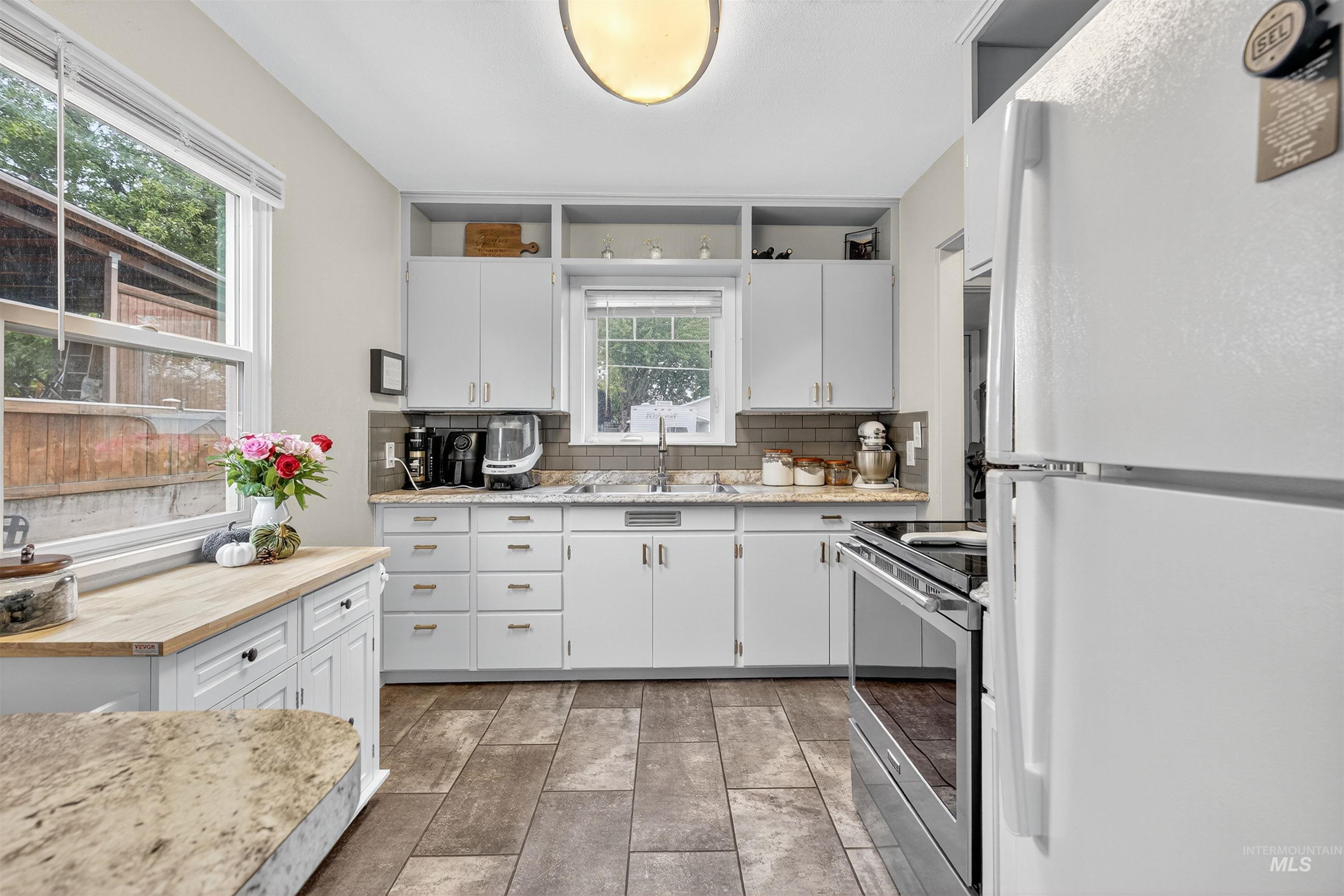Kitchen with freestanding refrigerator, butcher block counters, white cabinetry, stainless steel range with electric stovetop, and tasteful backsplash