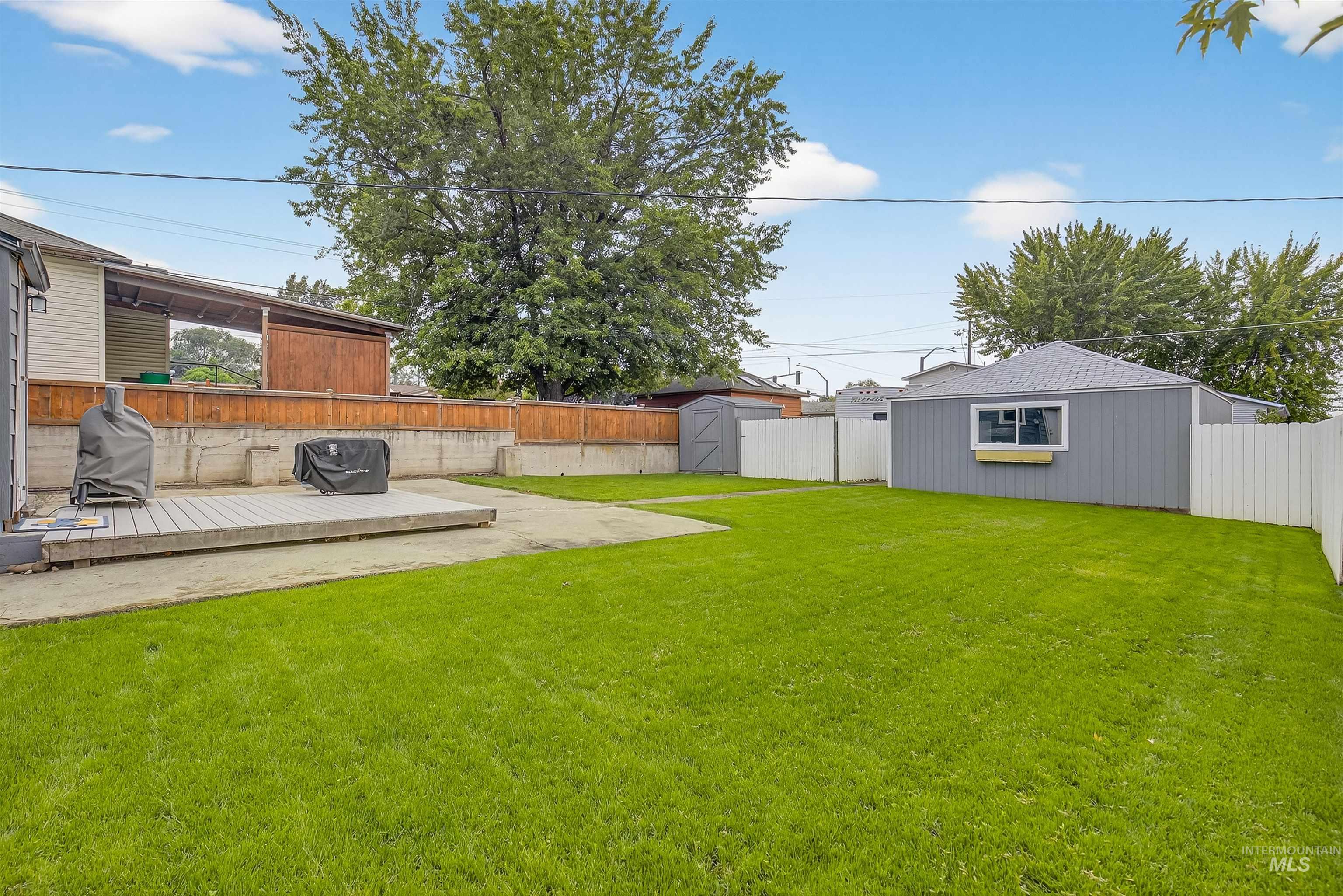Fenced backyard featuring a deck, a storage unit, and a patio area