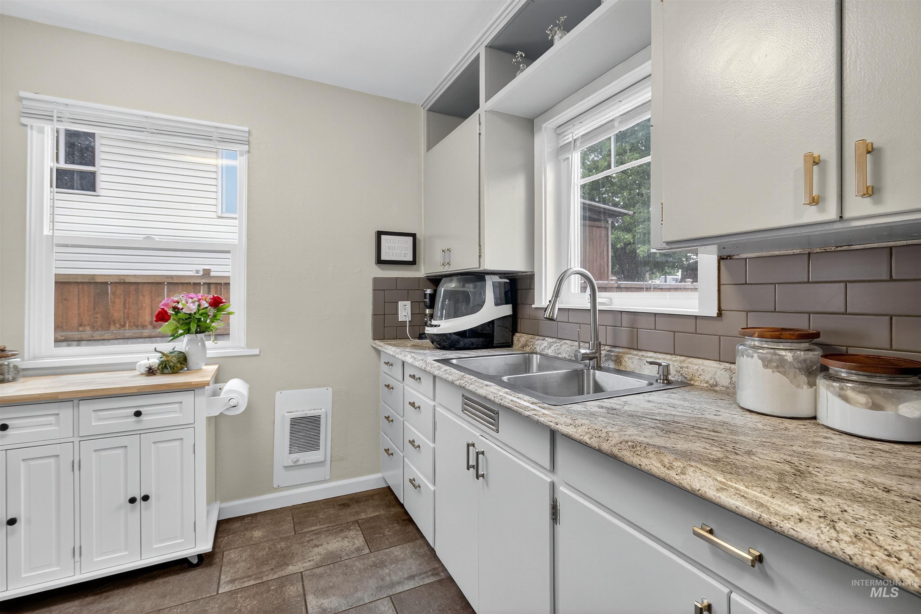 Kitchen with decorative backsplash, open shelves, white cabinets, and light stone countertops