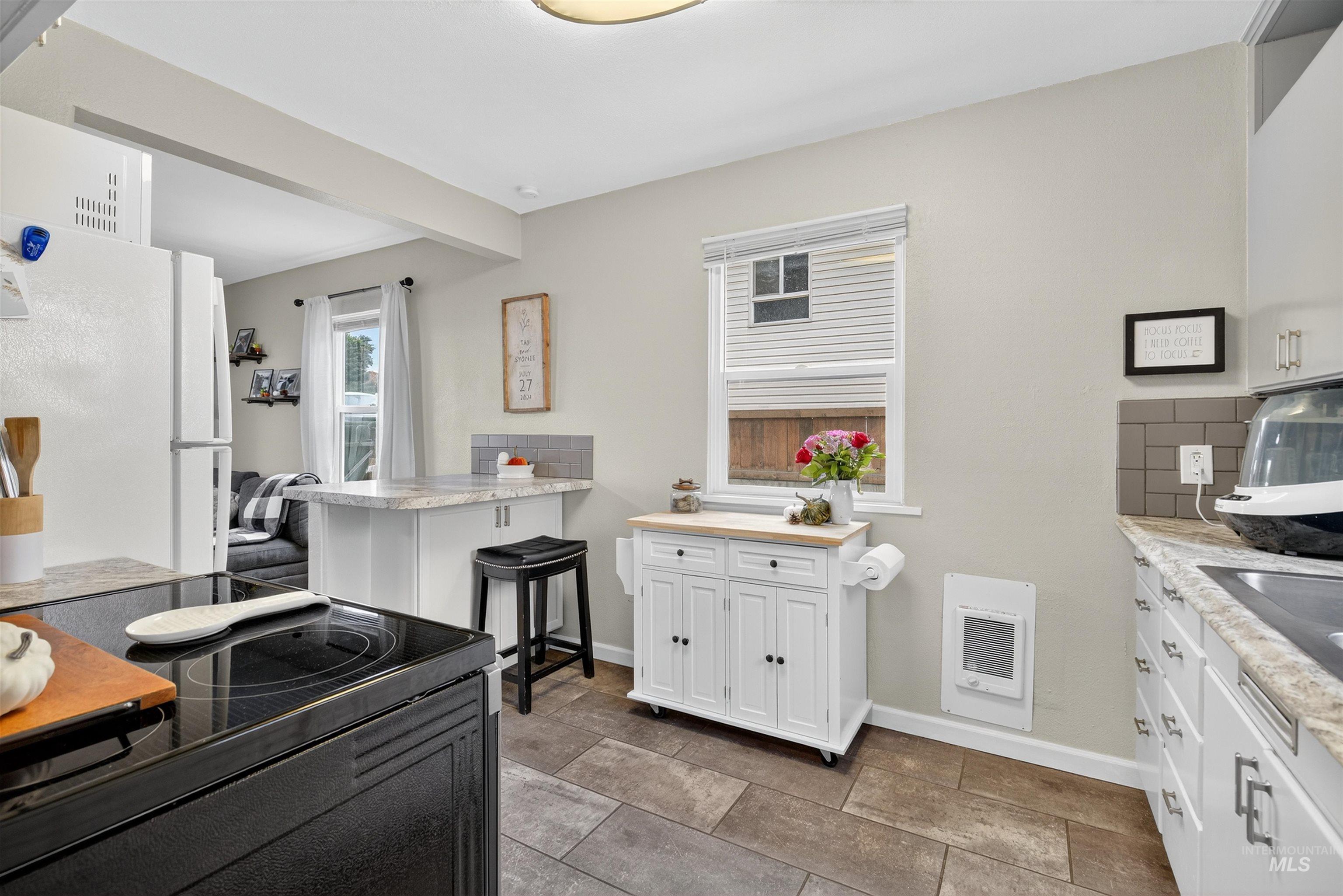 Kitchen with white cabinets, black electric range oven, freestanding refrigerator, a kitchen breakfast bar, and tasteful backsplash
