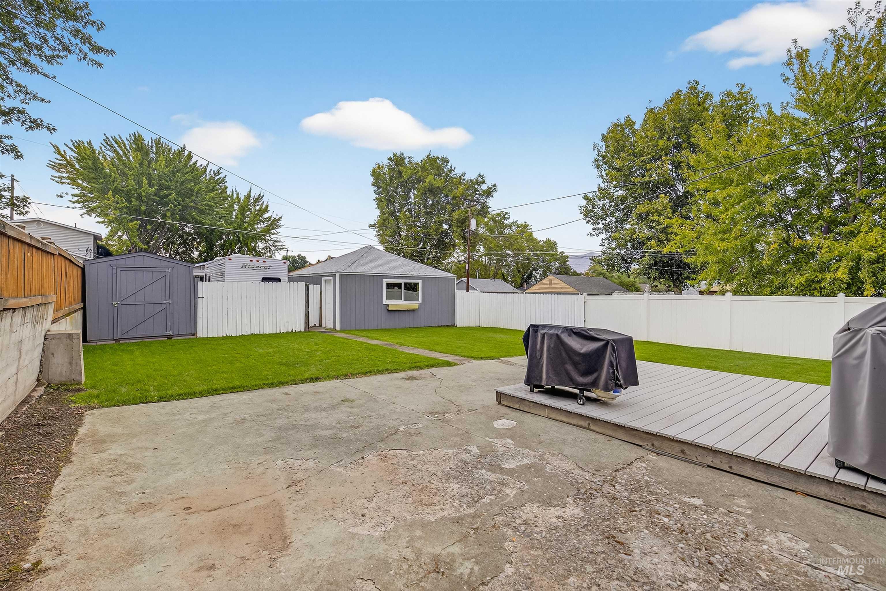 Fenced backyard featuring a wooden deck, grilling area, and an outdoor structure