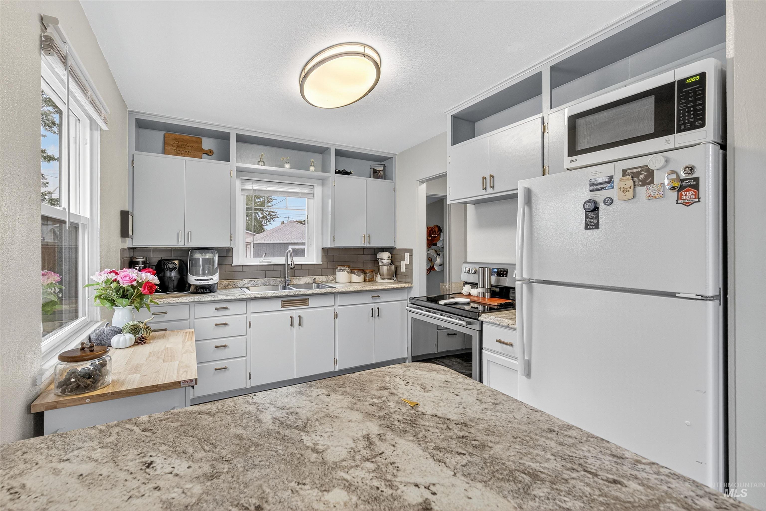 Kitchen with open shelves, white appliances, backsplash, white cabinets, and light stone counters