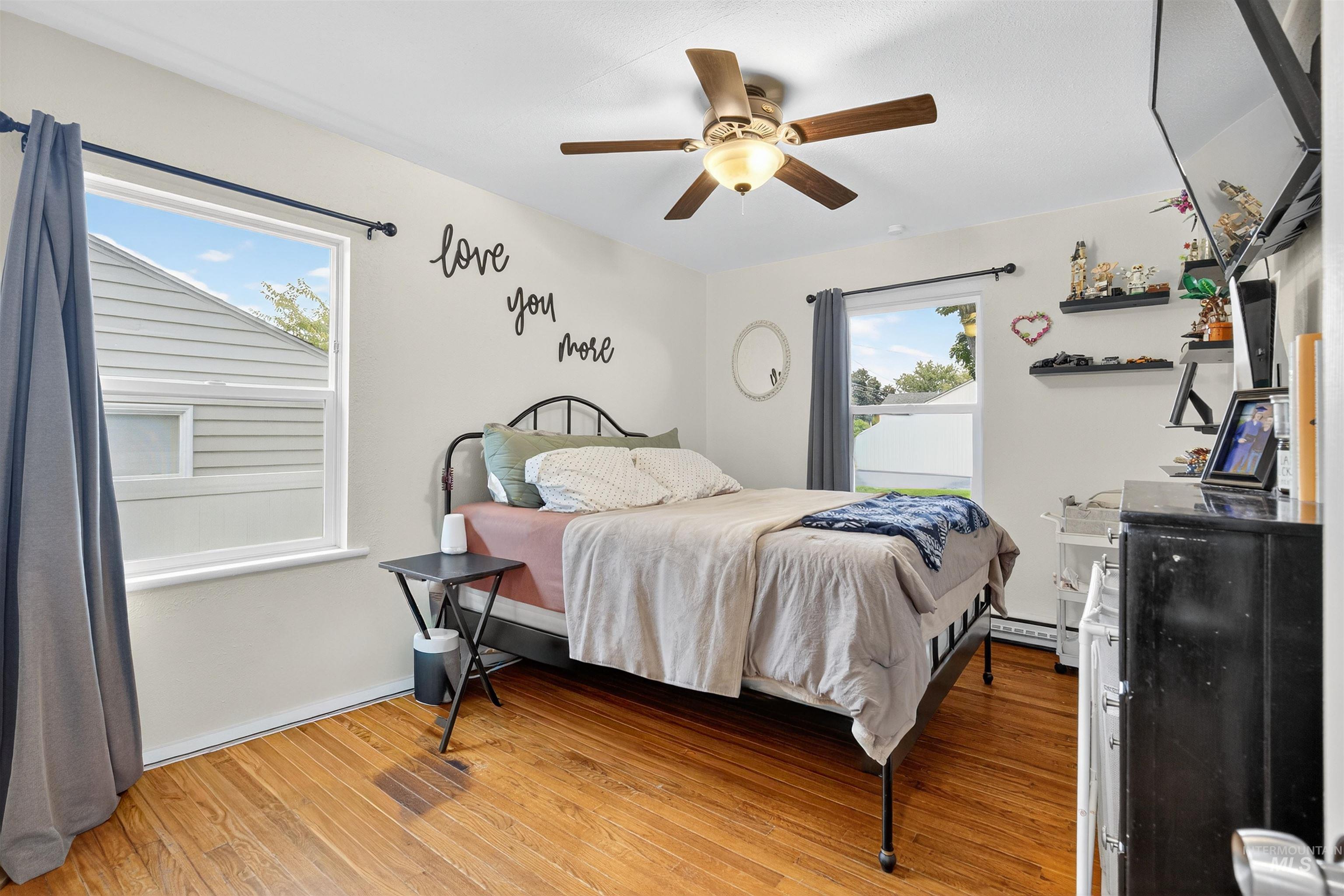 Bedroom featuring light wood-style flooring, multiple windows, a ceiling fan, and a baseboard heating unit