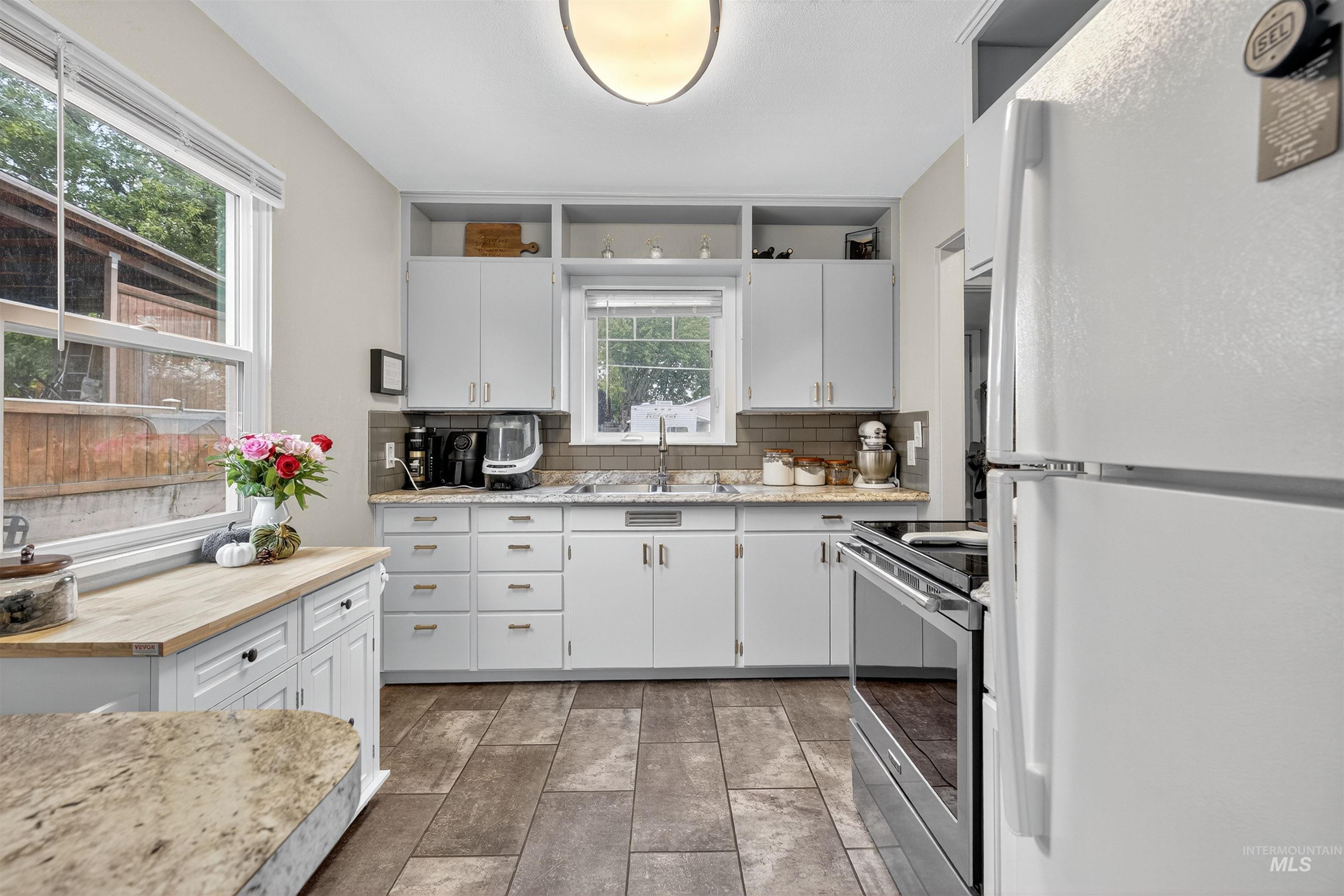 Kitchen featuring freestanding refrigerator, wooden counters, white cabinetry, electric range, and tasteful backsplash
