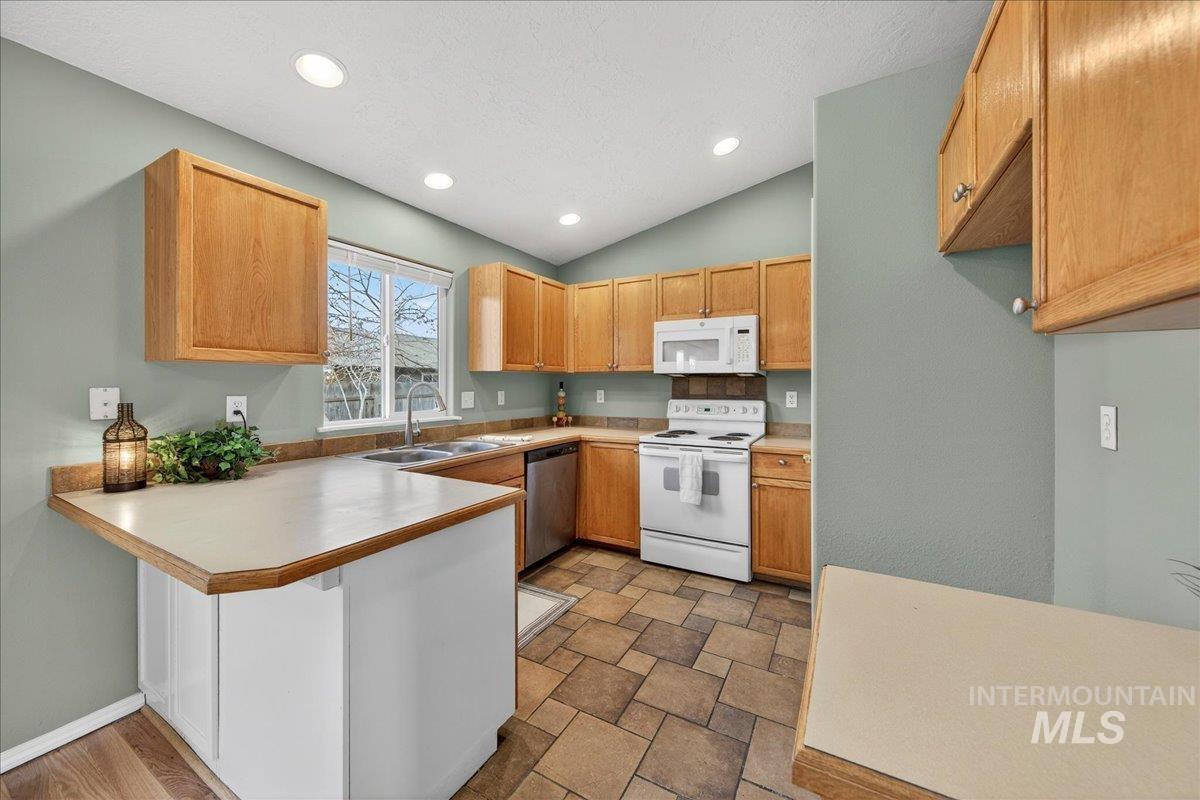 Kitchen featuring white appliances, light countertops, a peninsula, a breakfast bar area, and recessed lighting