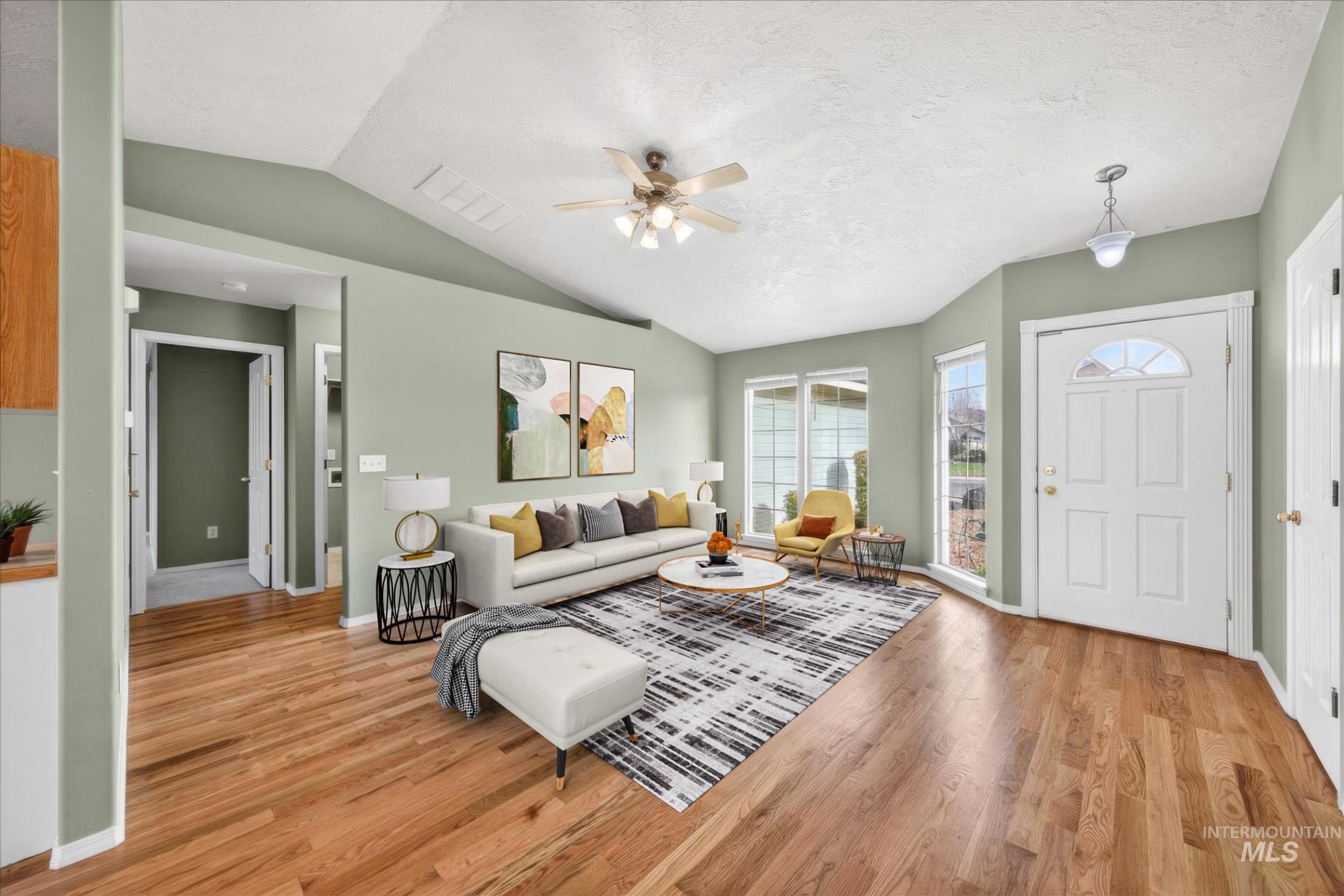Living room with ceiling fan, lofted ceiling, light wood-style flooring, and a textured ceiling