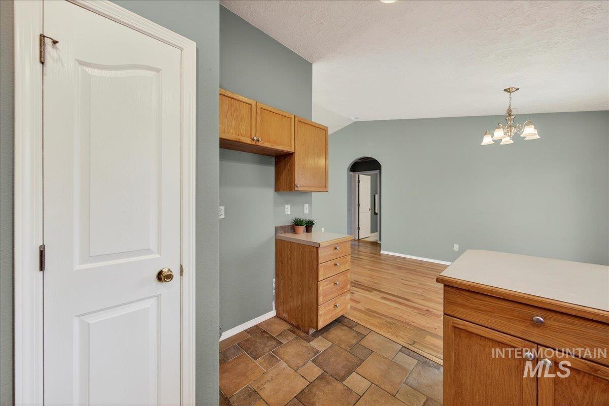 Kitchen featuring arched walkways, light countertops, decorative light fixtures, brown cabinets, and vaulted ceiling