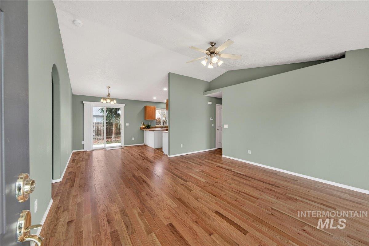 Unfurnished living room featuring wood finished floors, vaulted ceiling, a chandelier, ceiling fan, and a textured ceiling