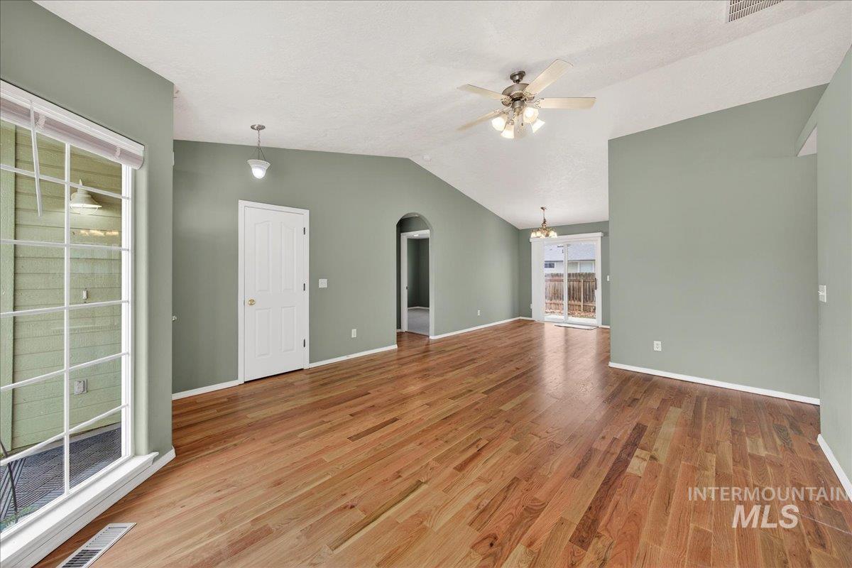 Unfurnished living room featuring arched walkways, lofted ceiling, light wood-style floors, a ceiling fan, and a textured ceiling