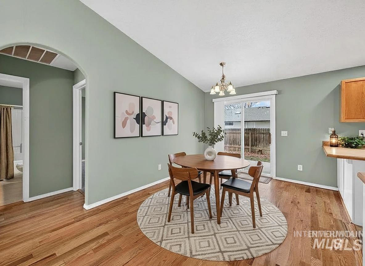 Dining space with vaulted ceiling, a chandelier, light wood-style floors, and arched walkways