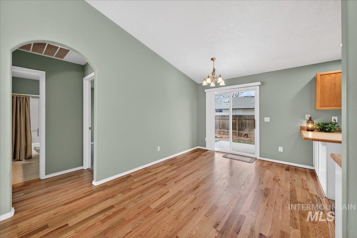 Unfurnished dining area with vaulted ceiling, a chandelier, light wood-style flooring, and arched walkways