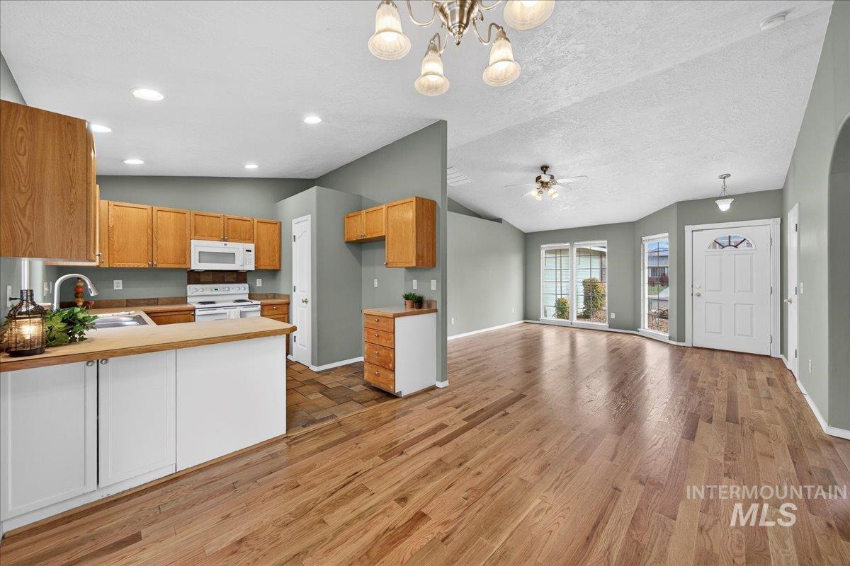 Kitchen with decorative light fixtures, vaulted ceiling, white appliances, open floor plan, and a chandelier