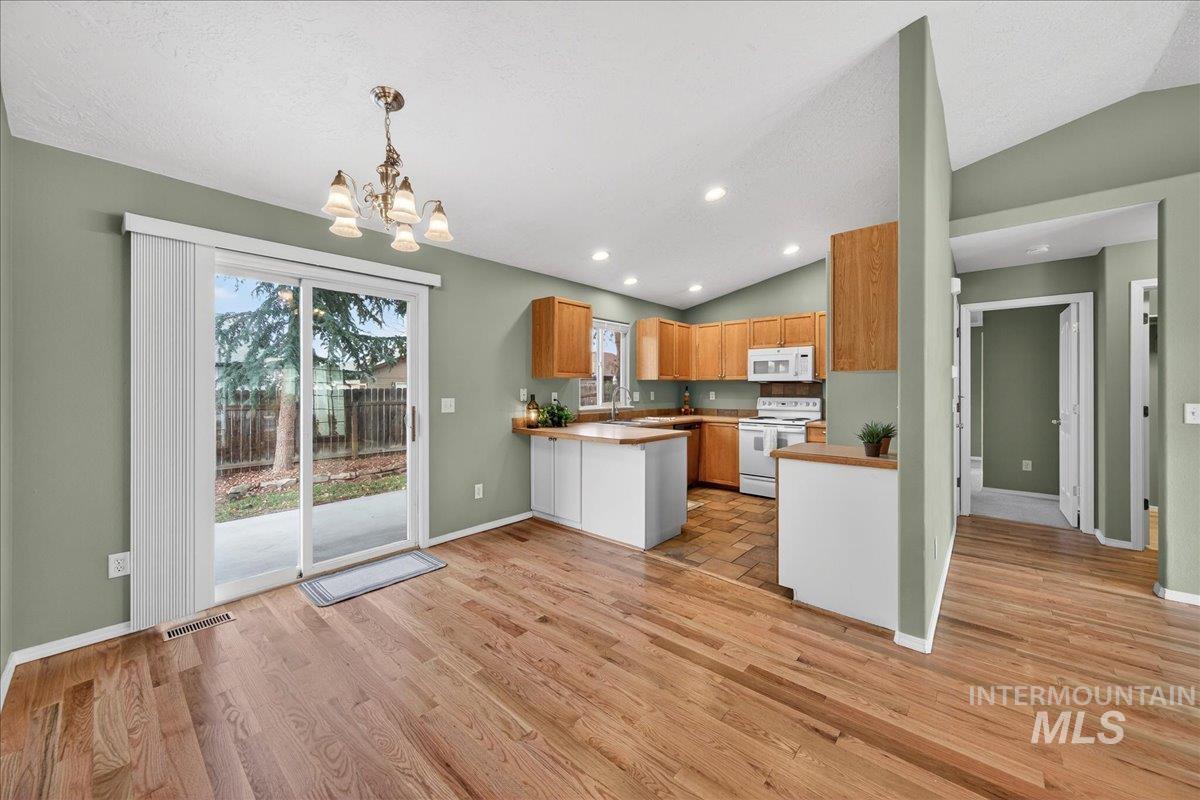 Kitchen featuring lofted ceiling, white appliances, recessed lighting, decorative light fixtures, and light countertops