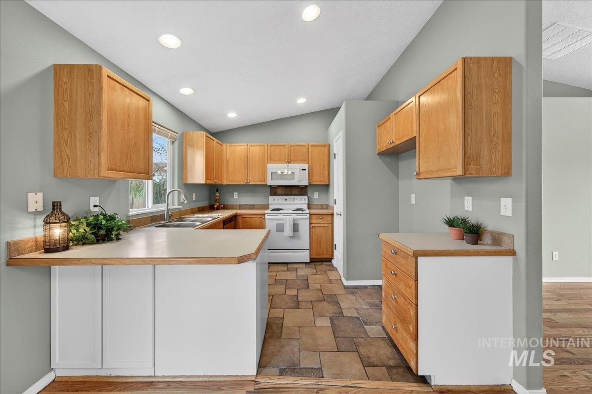 Kitchen with light countertops, white appliances, a peninsula, stone finish flooring, and recessed lighting