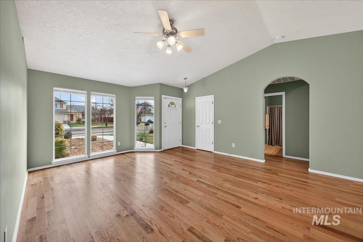 Unfurnished living room with light wood-style floors, a textured ceiling, ceiling fan, arched walkways, and lofted ceiling
