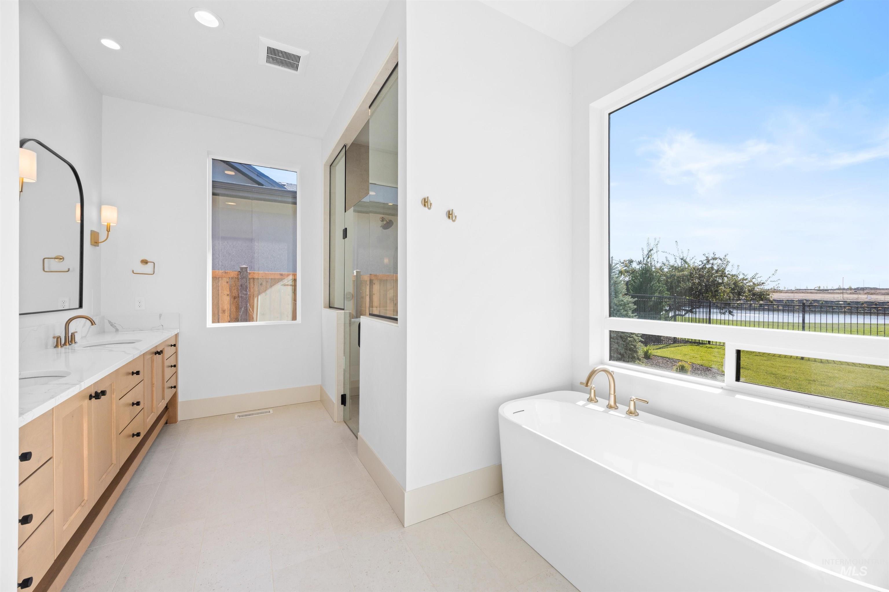 Bathroom featuring double vanity, a freestanding tub, a stall shower, recessed lighting, and a water view