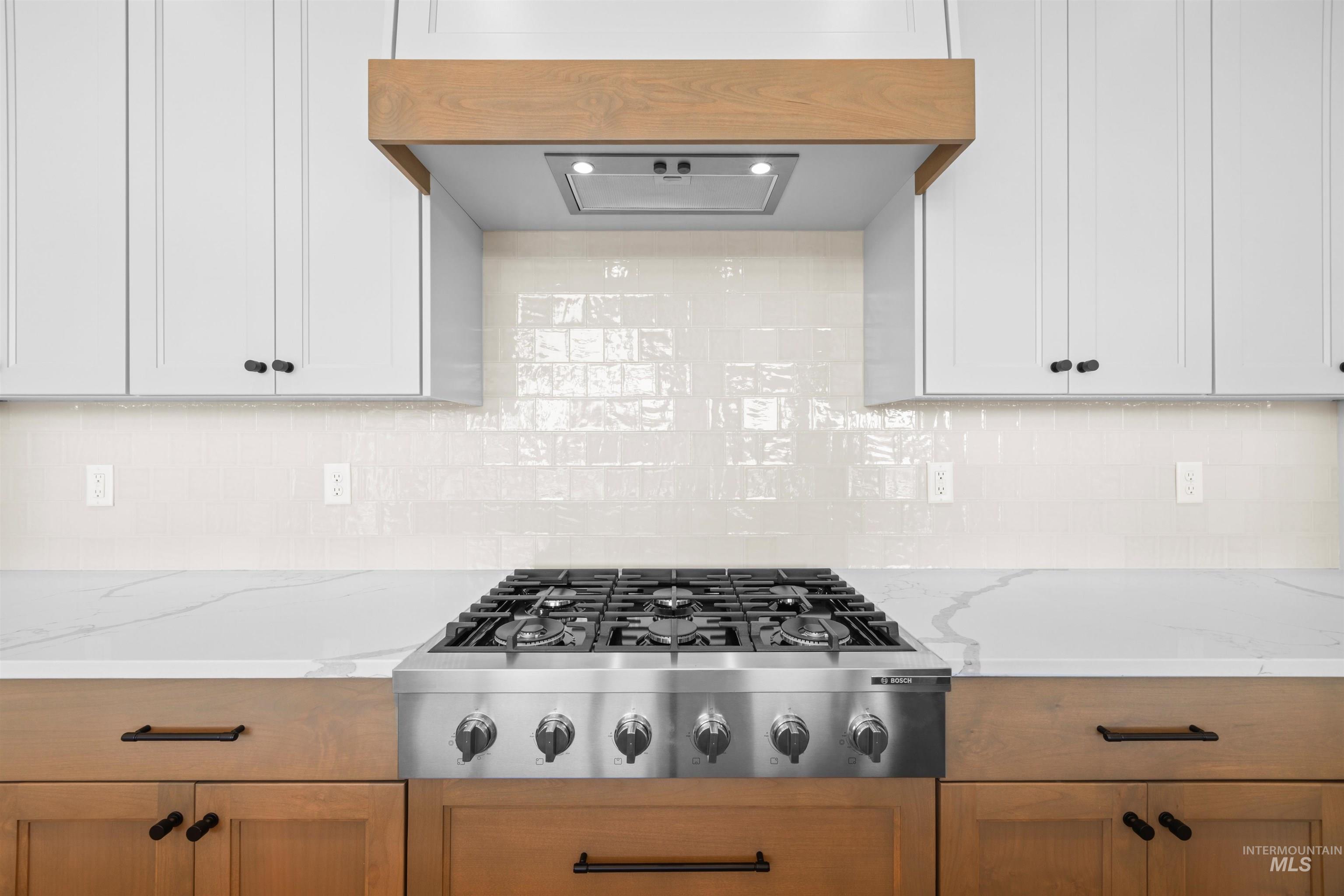 Kitchen with ventilation hood, stainless steel gas stovetop, tasteful backsplash, and light stone countertops