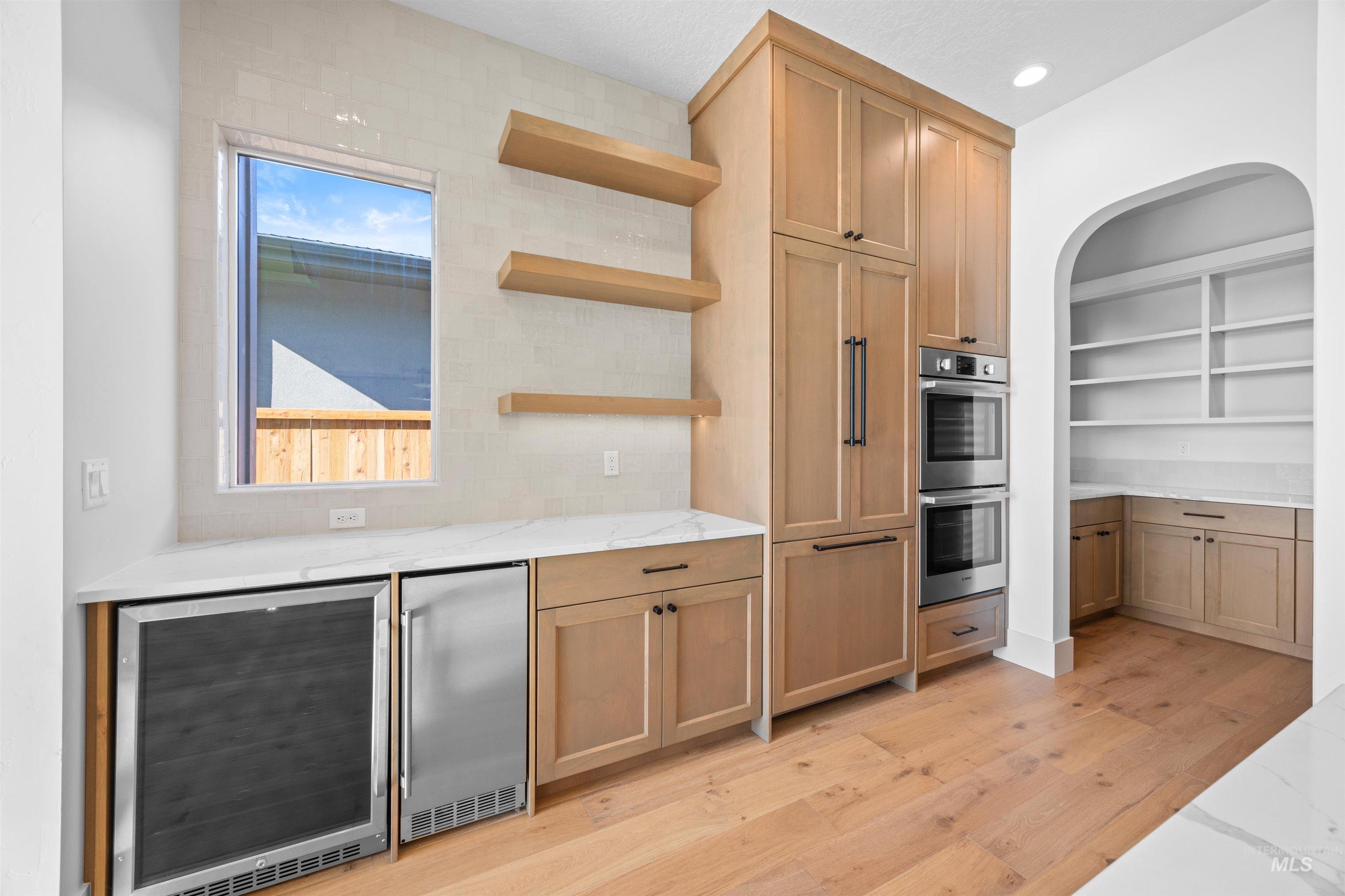 Kitchen with open shelves, beverage cooler, stainless steel appliances, light stone countertops, and recessed lighting
