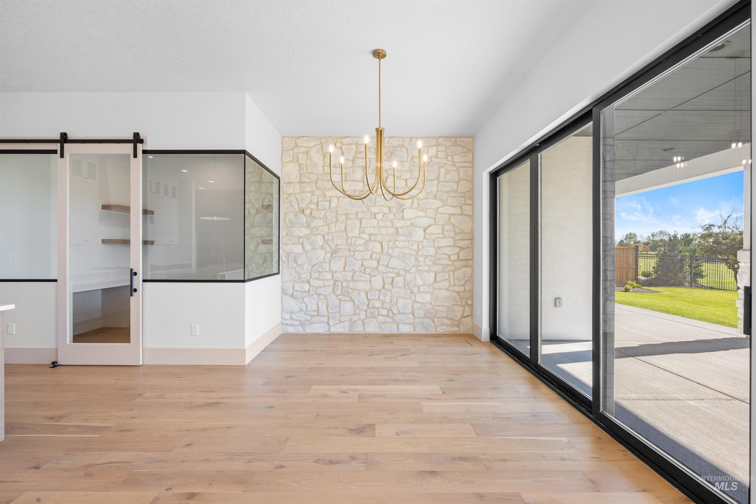 Unfurnished dining area with a barn door, light wood-type flooring, and a chandelier