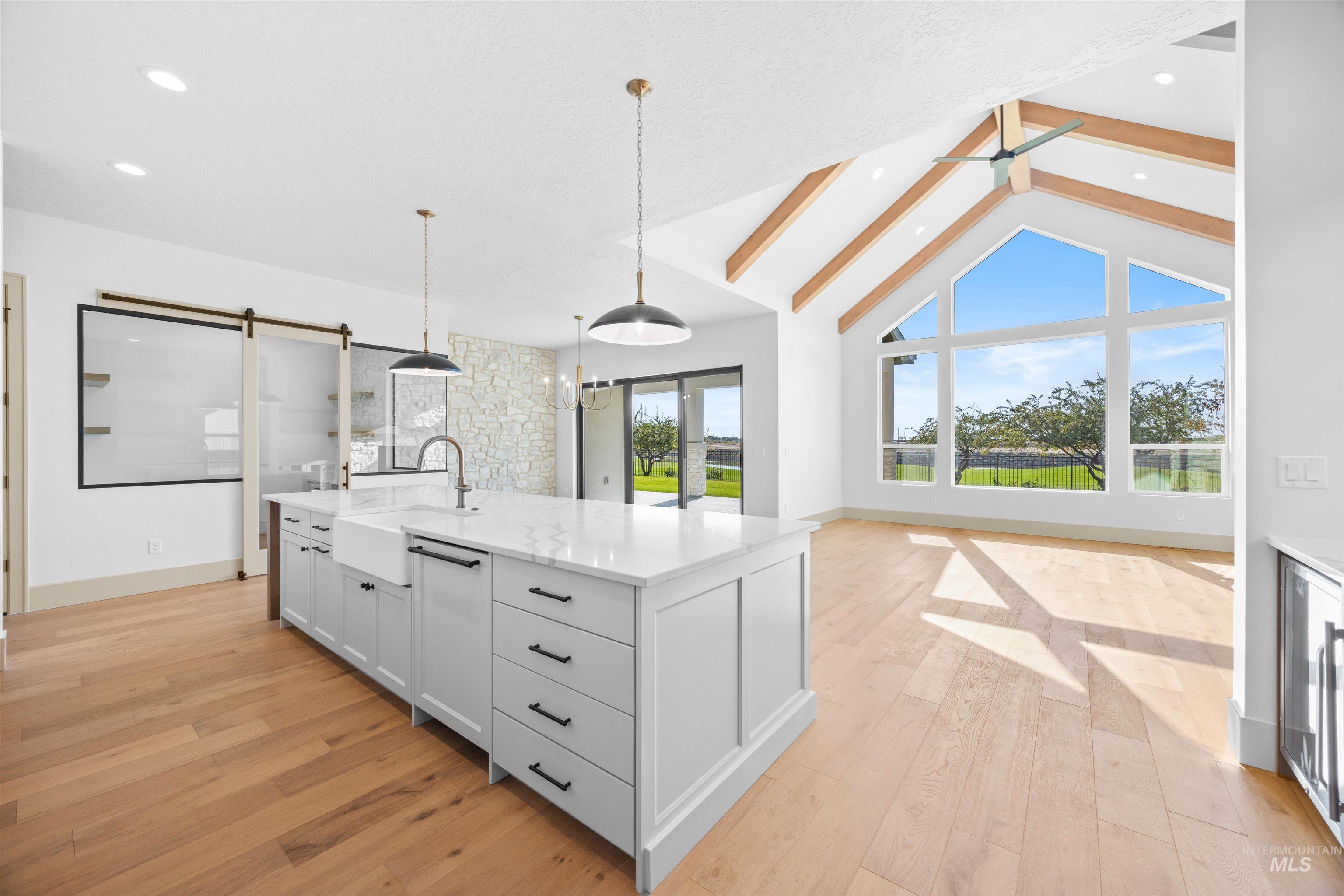 Kitchen featuring light stone countertops, decorative light fixtures, beamed ceiling, light wood finished floors, and an island with sink