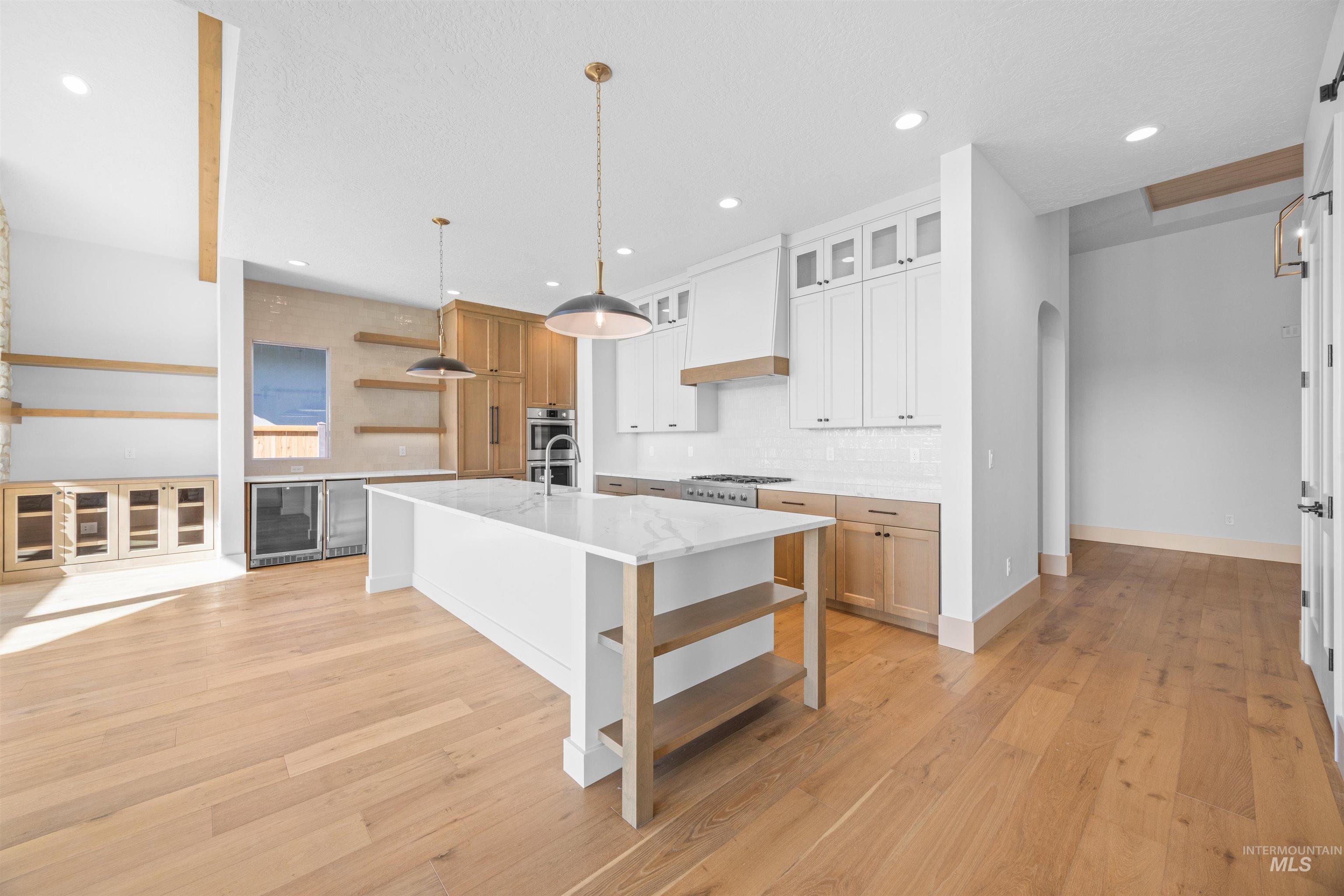 Kitchen featuring open shelves, hanging light fixtures, arched walkways, light wood-style flooring, and a kitchen island with sink