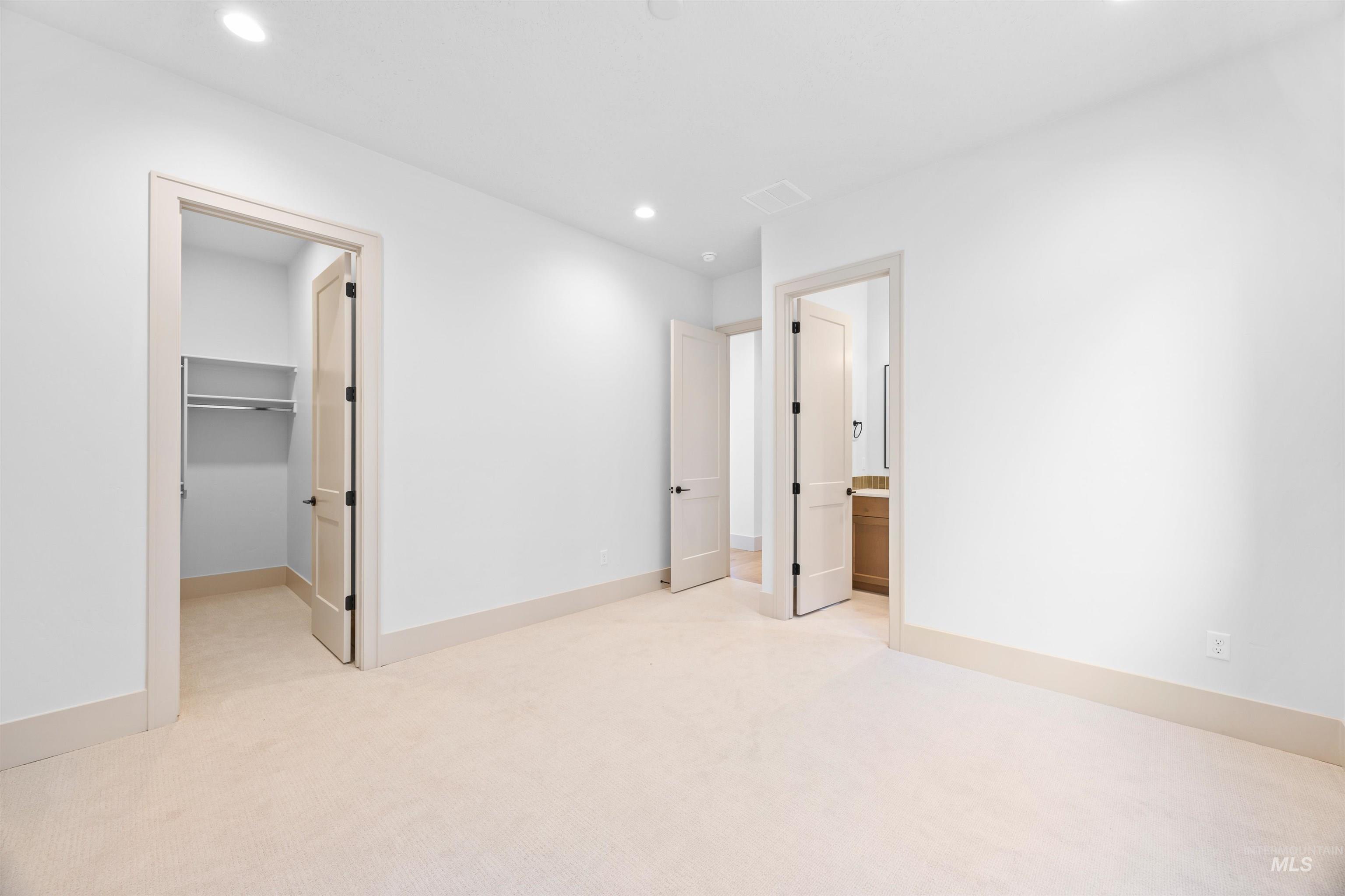Unfurnished bedroom with a spacious closet, light carpet, recessed lighting, and ensuite bathroom