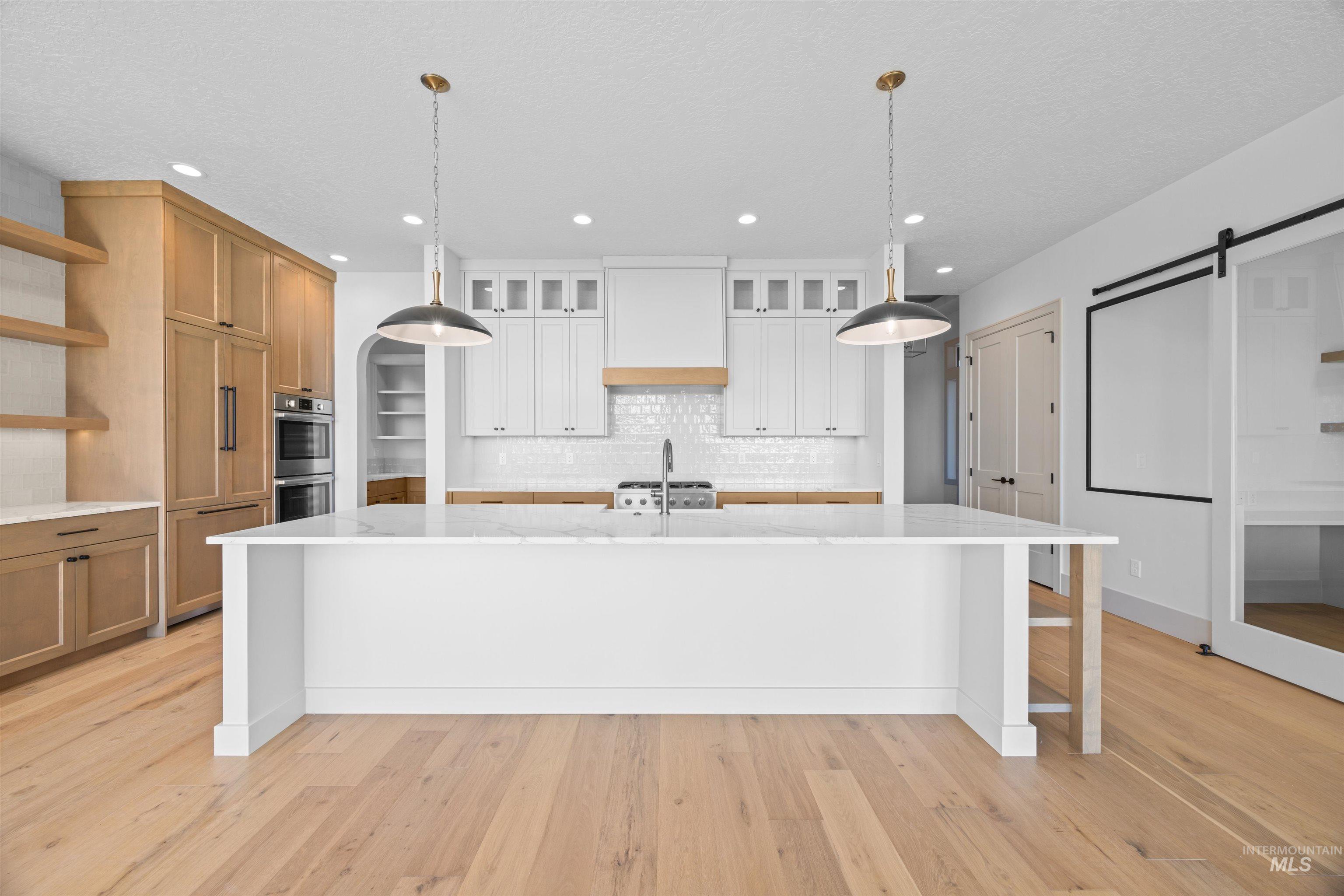 Kitchen featuring a barn door, tasteful backsplash, decorative light fixtures, light stone countertops, and open shelves