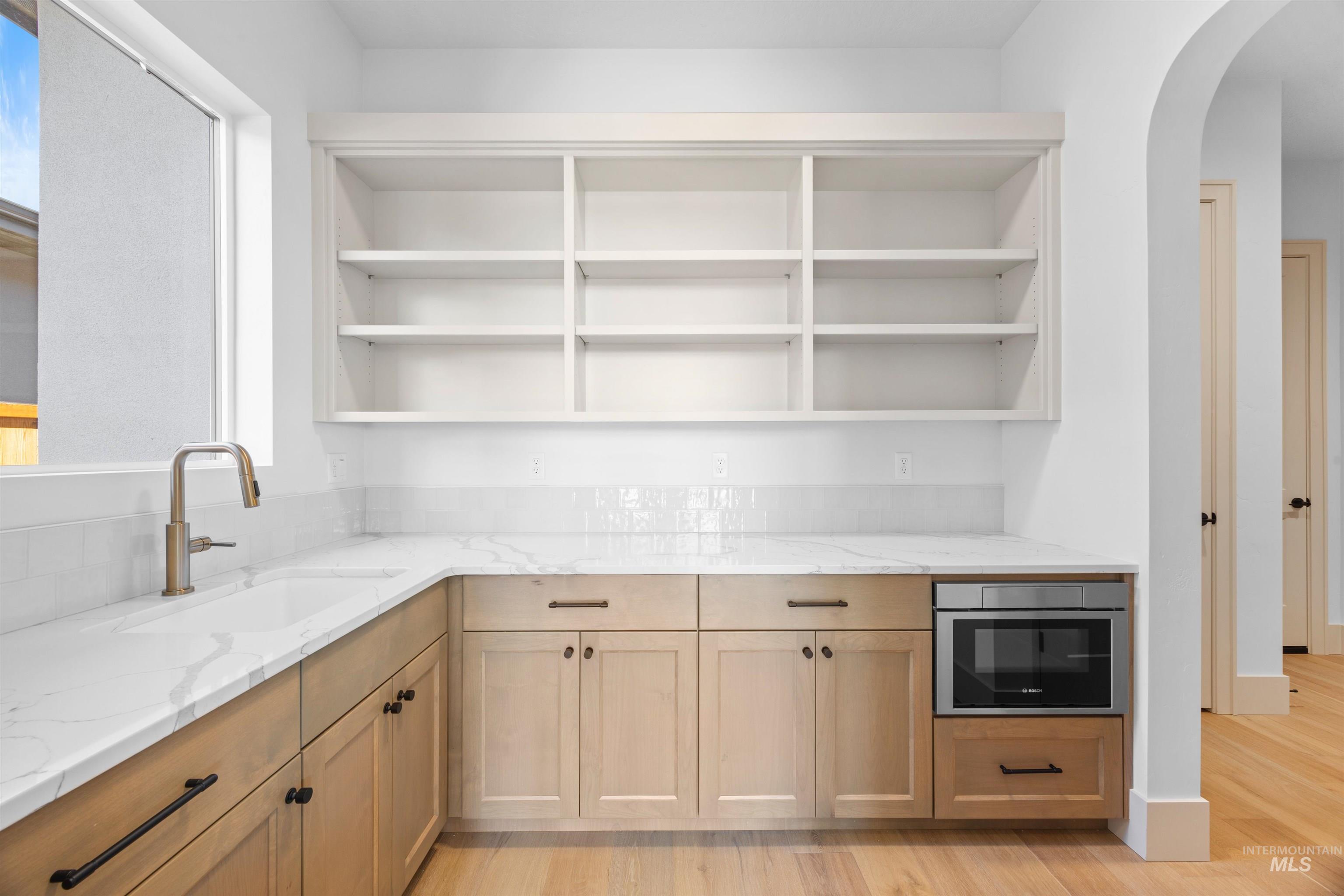 Kitchen featuring light stone counters, arched walkways, light wood-style floors, open shelves, and light brown cabinets