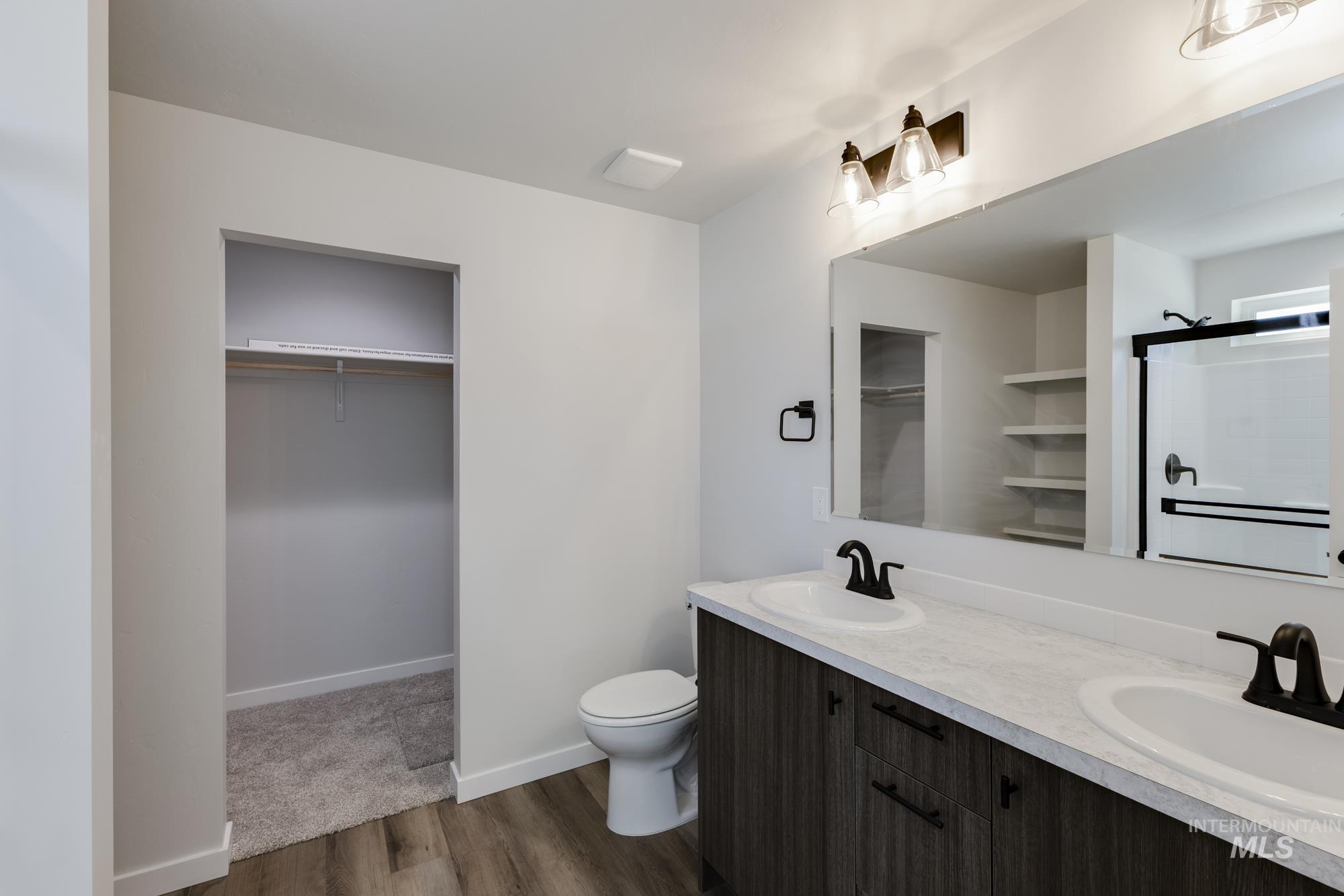 Full bath featuring a spacious closet, double vanity, dark wood finished floors, and a stall shower