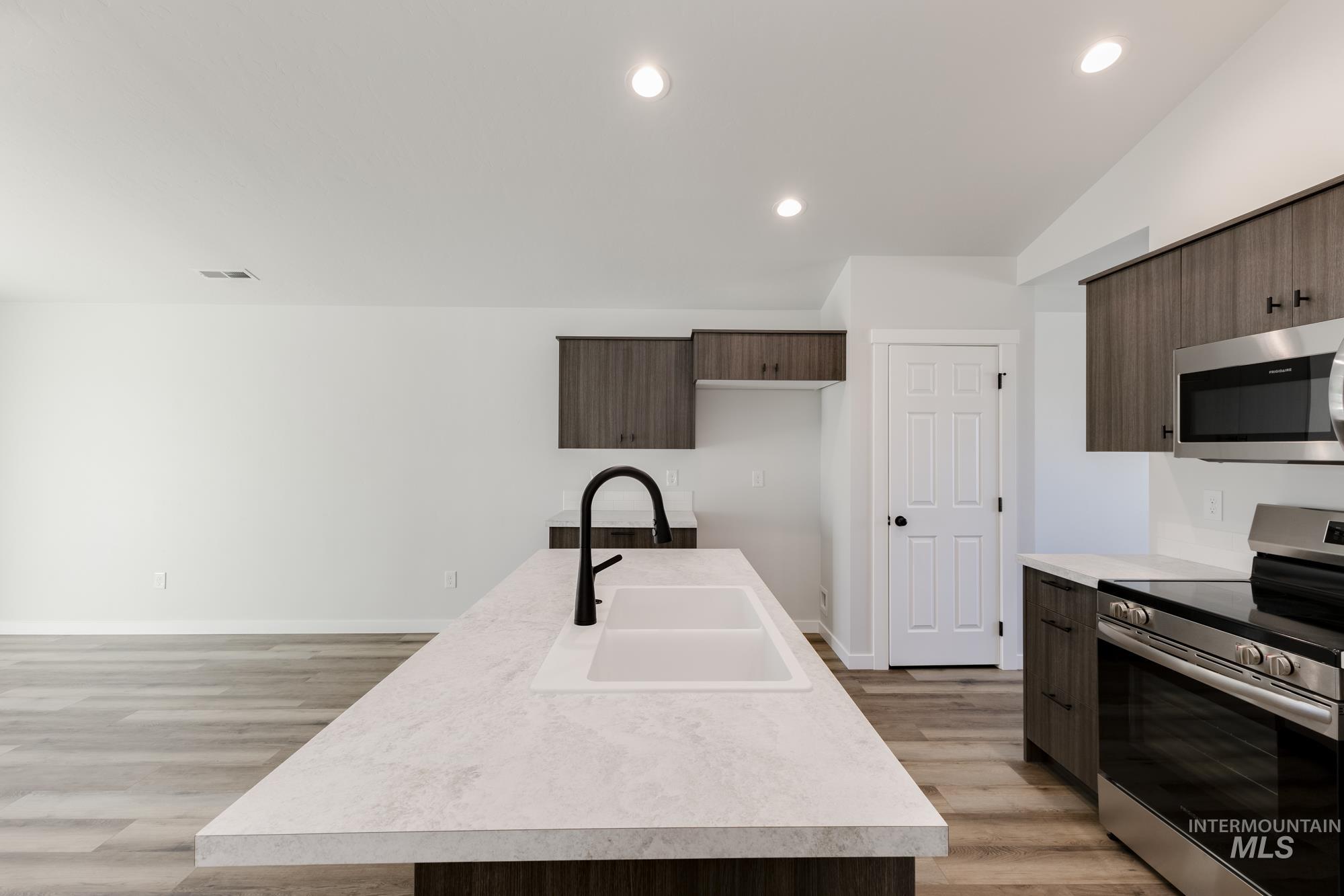Kitchen featuring stainless steel appliances, light countertops, recessed lighting, light wood finished floors, and a center island with sink