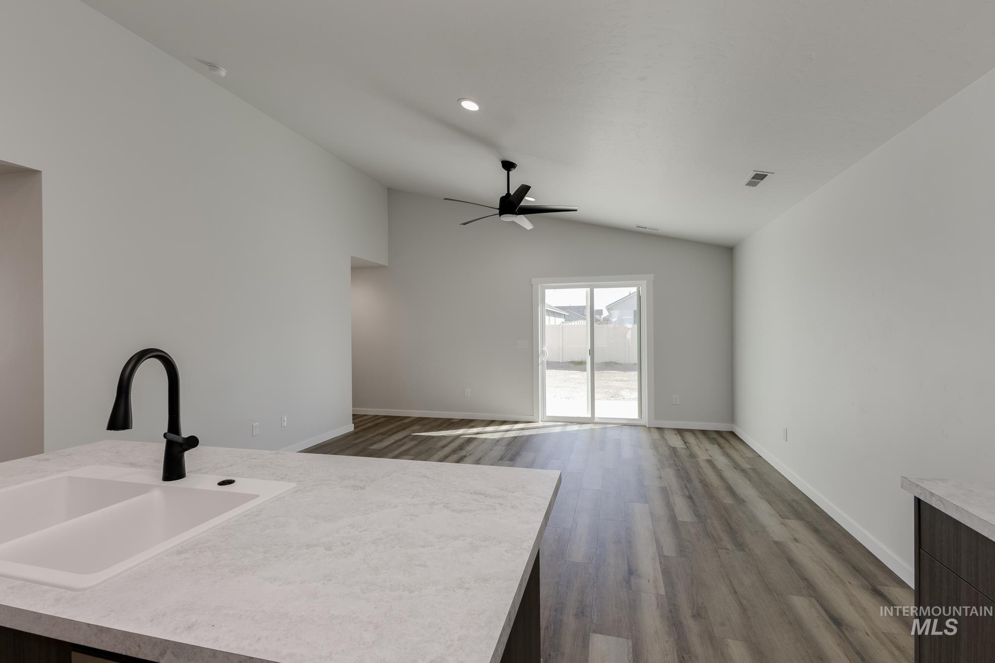 Kitchen with light countertops, wood finished floors, vaulted ceiling, open floor plan, and an island with sink