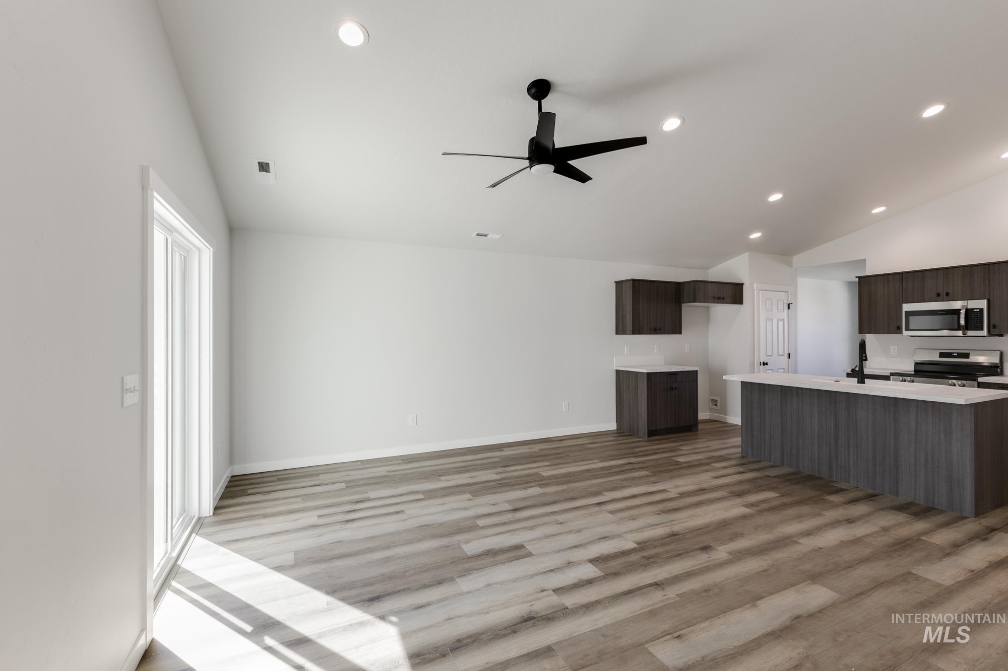 Kitchen with vaulted ceiling, light wood-style flooring, dark brown cabinetry, stainless steel appliances, and open floor plan