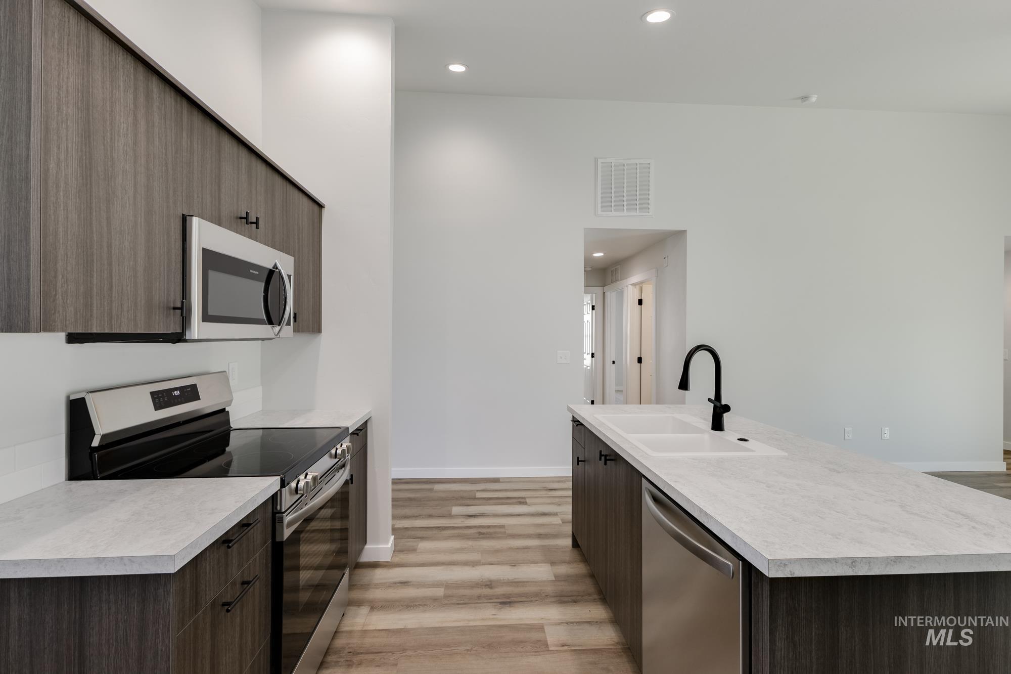 Kitchen featuring appliances with stainless steel finishes, dark brown cabinets, modern cabinets, recessed lighting, and light countertops
