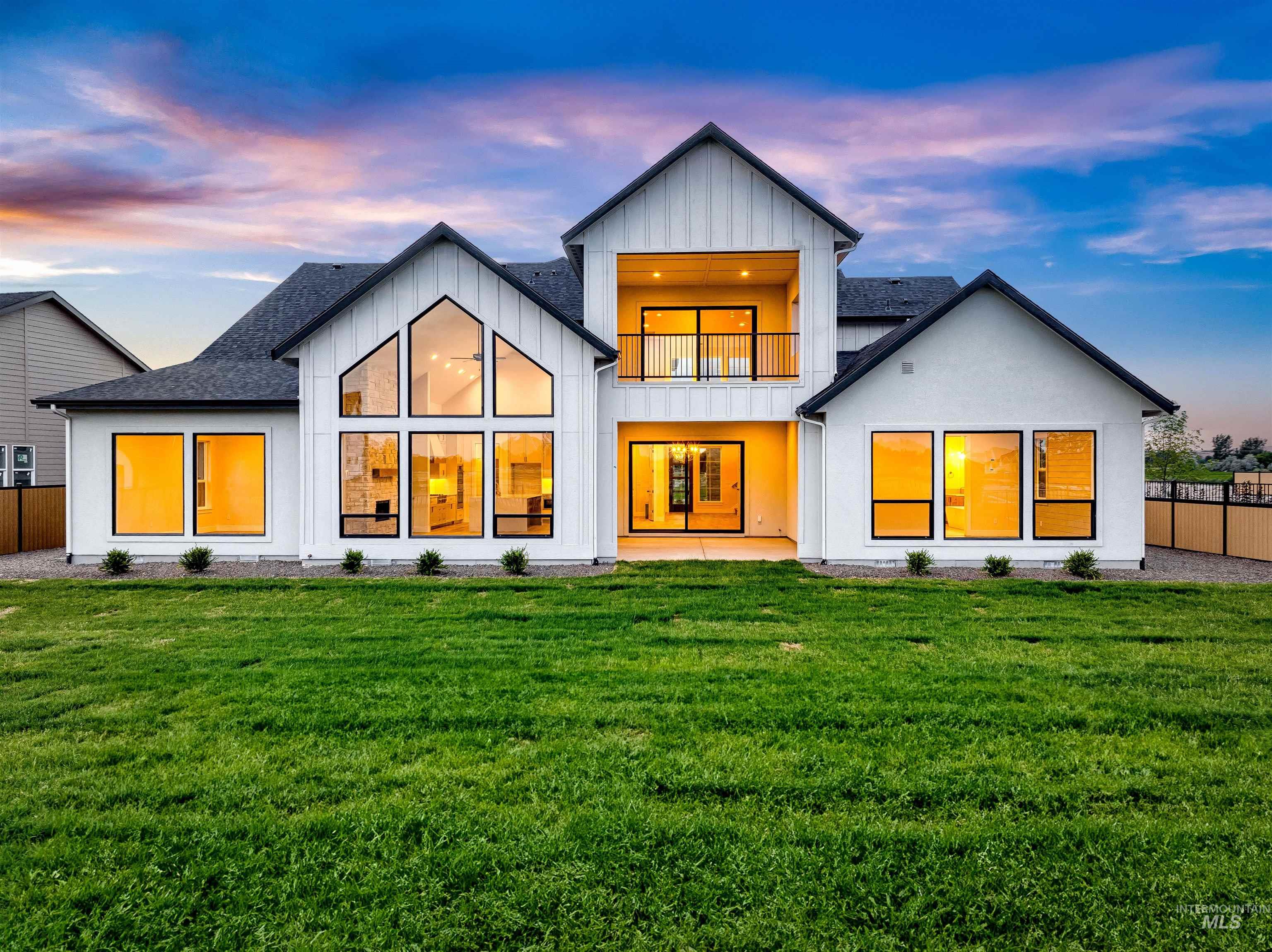 Back of property at dusk featuring board and batten siding, a balcony, a patio area, and a shingled roof