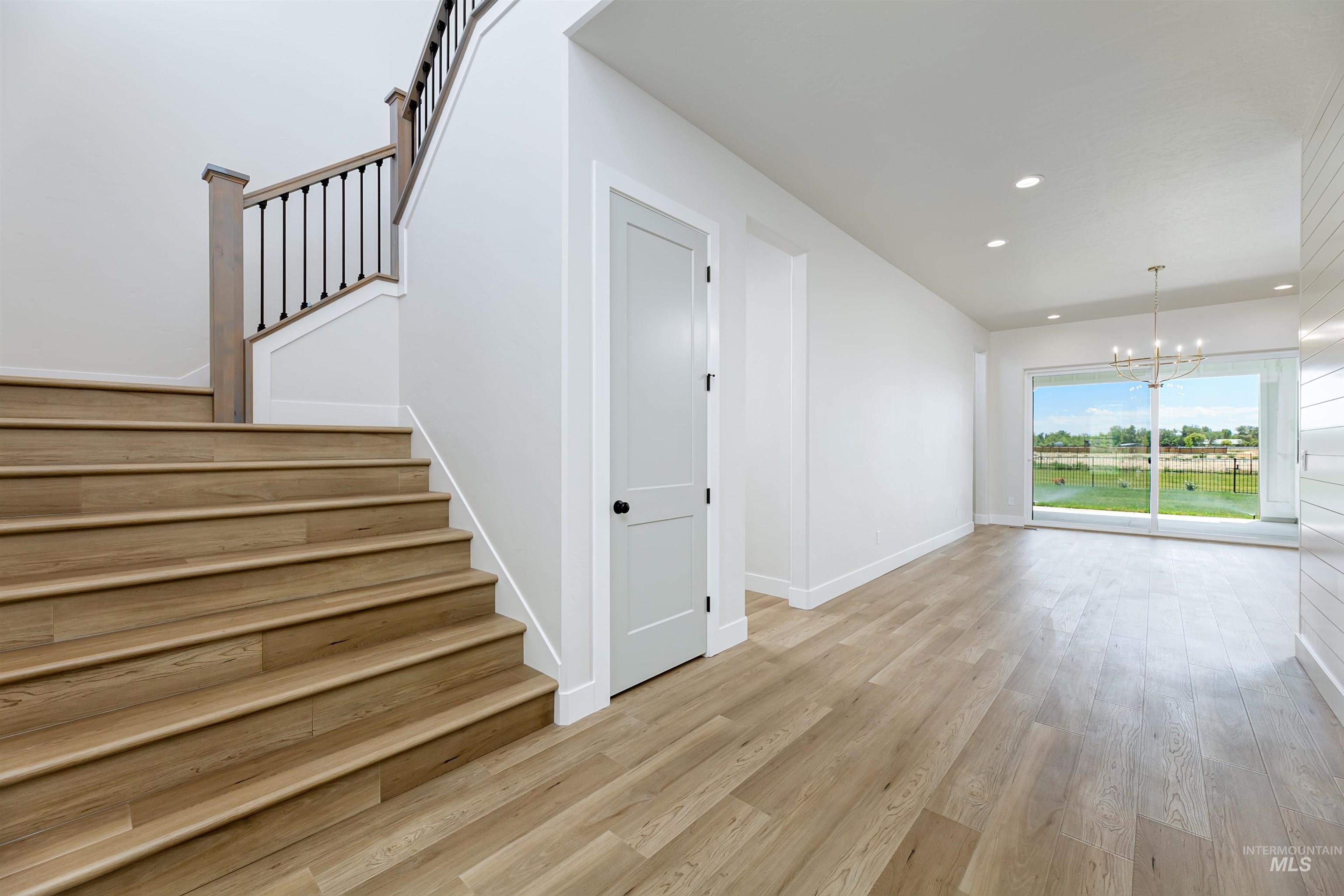 Unfurnished living room featuring light wood-type flooring, recessed lighting, a chandelier, and stairway