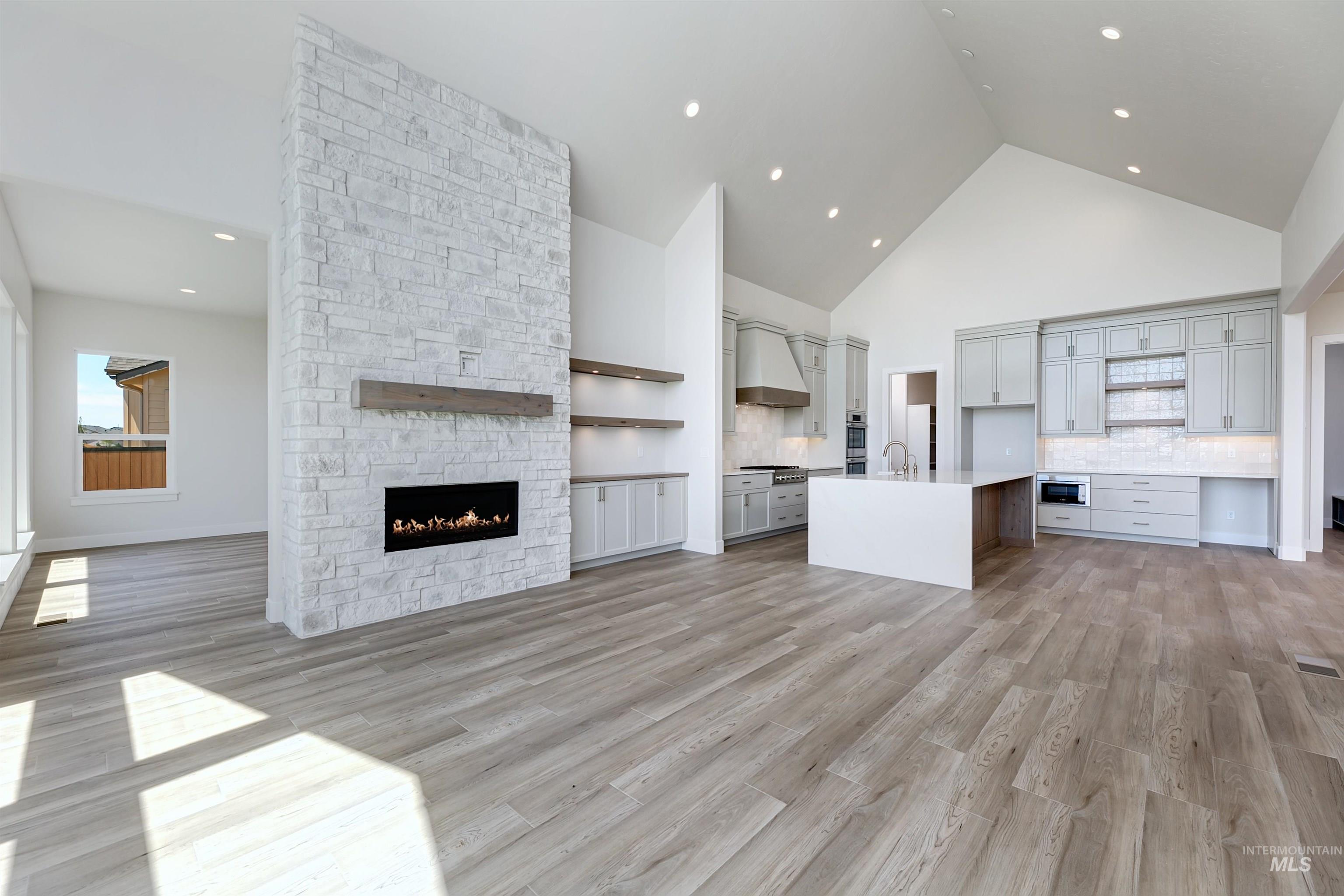 Unfurnished living room featuring high vaulted ceiling, a stone fireplace, light wood-style flooring, and recessed lighting