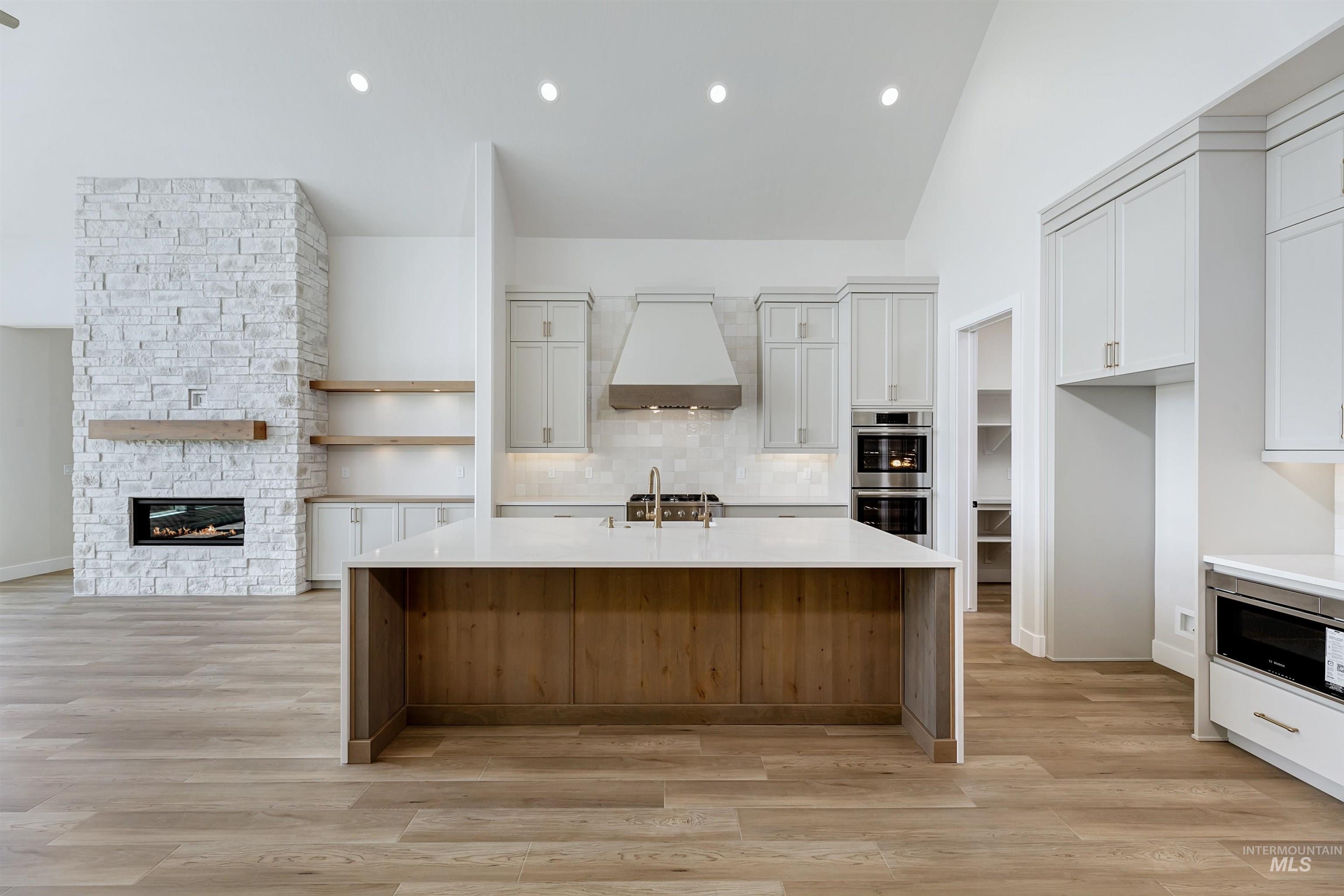 Kitchen featuring light stone countertops, backsplash, custom range hood, a fireplace, and light wood-style floors