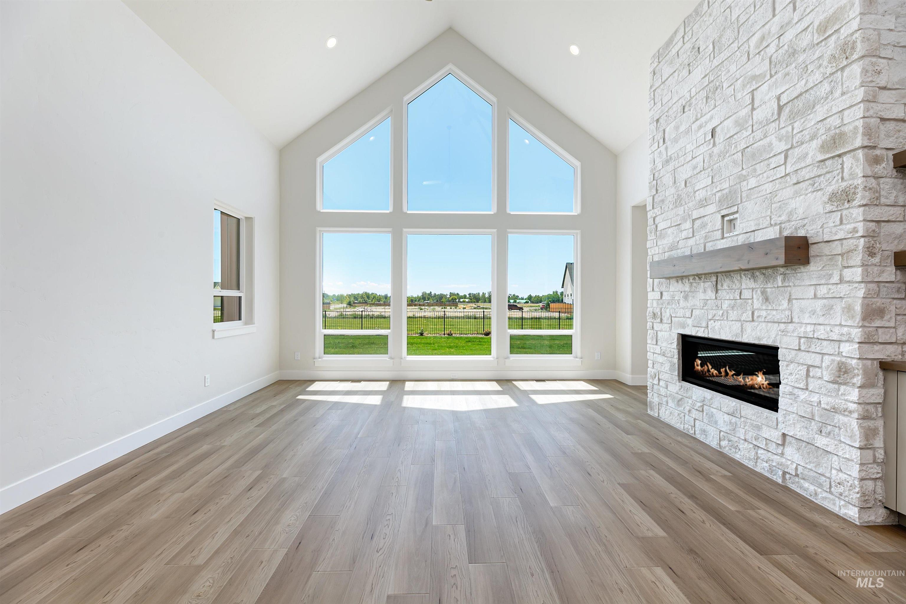 Unfurnished living room with high vaulted ceiling, light wood-style floors, and a stone fireplace