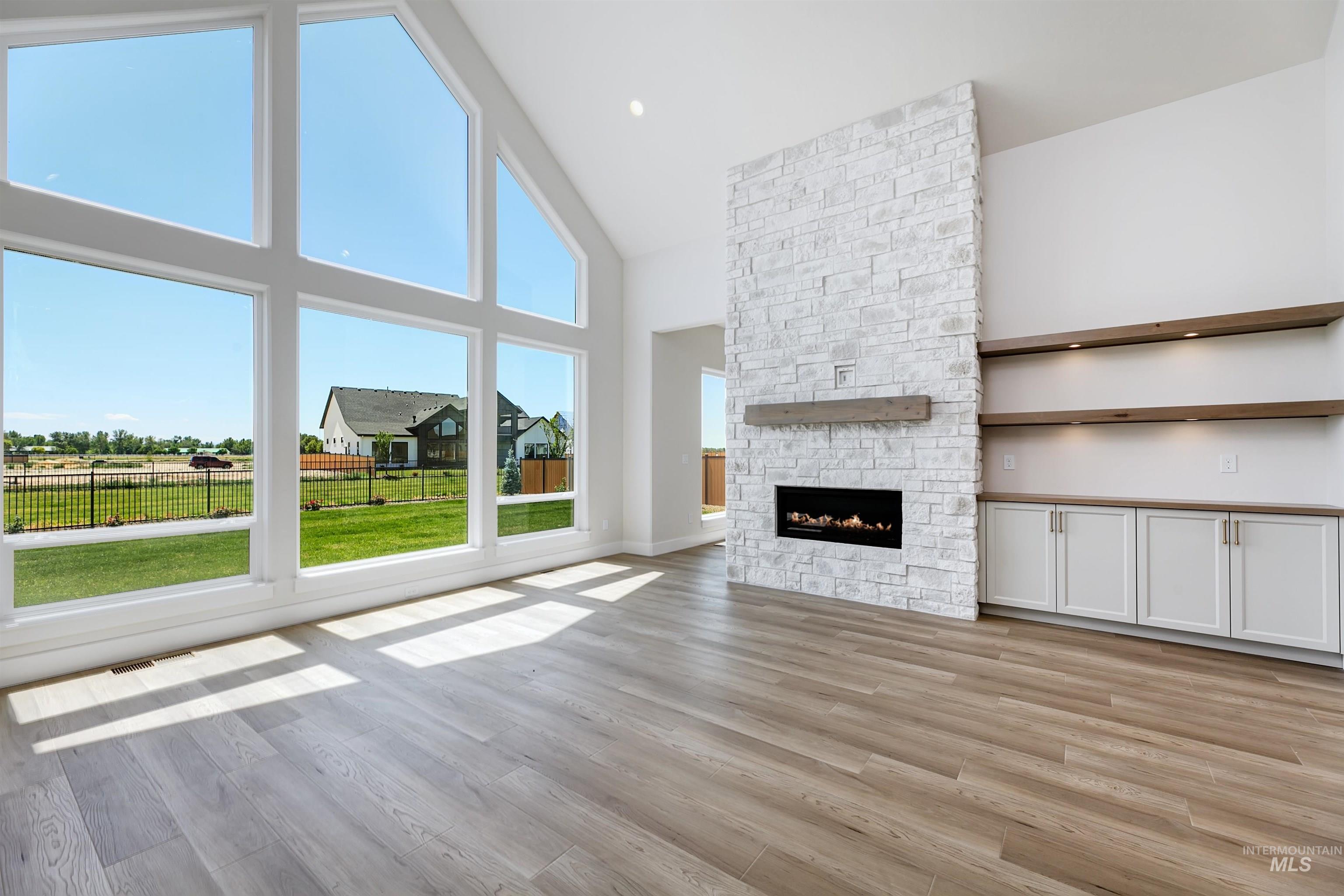 Unfurnished living room with high vaulted ceiling, light wood finished floors, and a stone fireplace